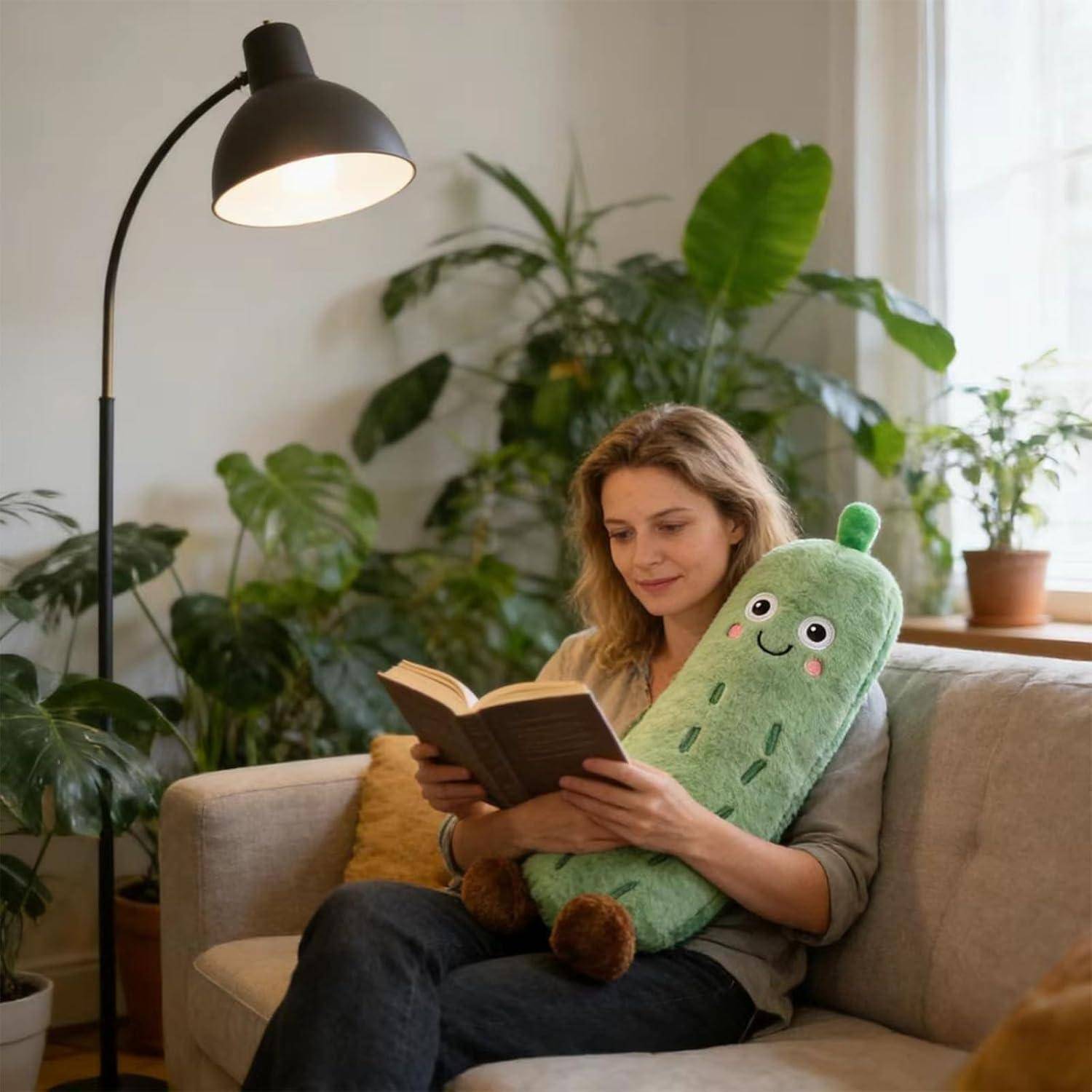 Frau liest ein Buch auf einem Sofa, während sie ein weiches Kaktuskissen hält, mit einer Stehlampe und Zimmerpflanzen in einem gemütlichen Wohnzimmer.