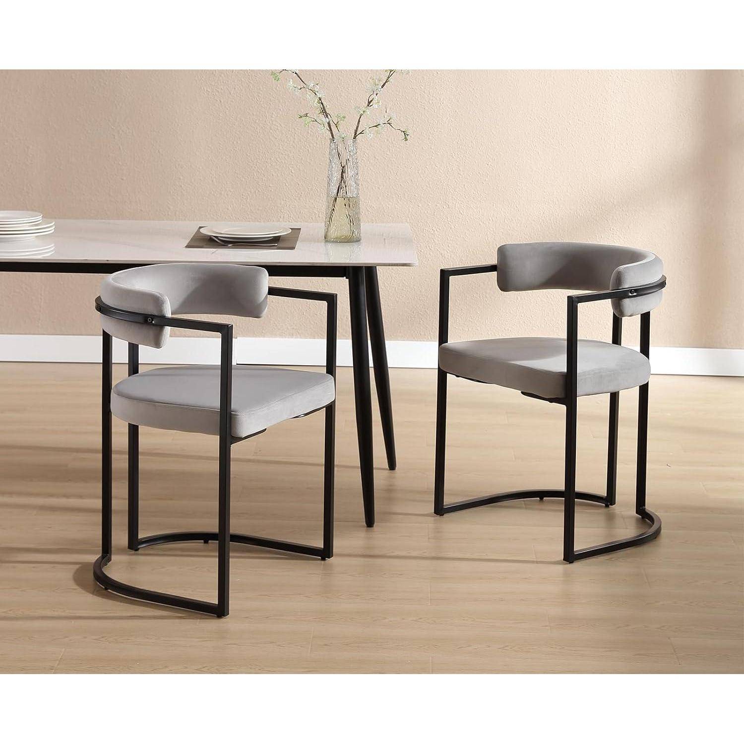 Zwei moderne grau gepolsterte Stühle mit schwarzen Metallrahmen neben einem Esstisch in einem minimalistischen Raum.