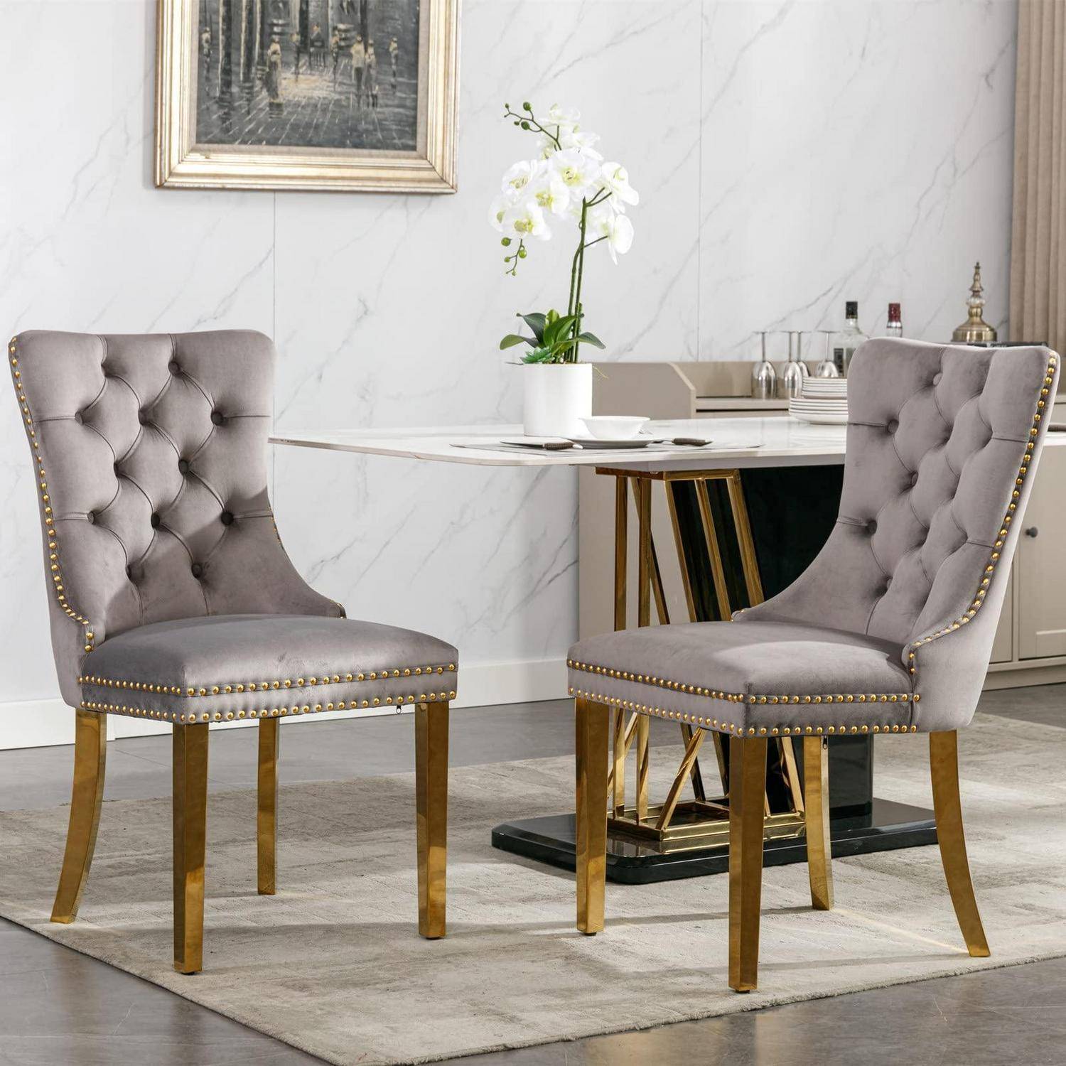 Zwei graue gepolsterte Esszimmerstühle mit goldenen Beinen neben einem modernen Marmortisch in einem hellen, eleganten Essbereich.