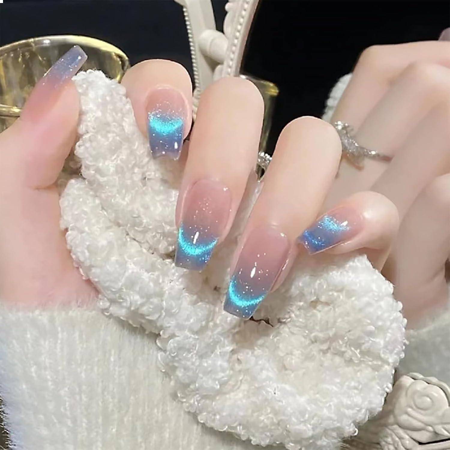 Nahaufnahme von gepflegten Händen mit langen glitzernden rosa-blauen Ombré-Nägeln, die auf einem flauschigen weißen Accessoire ruhen.