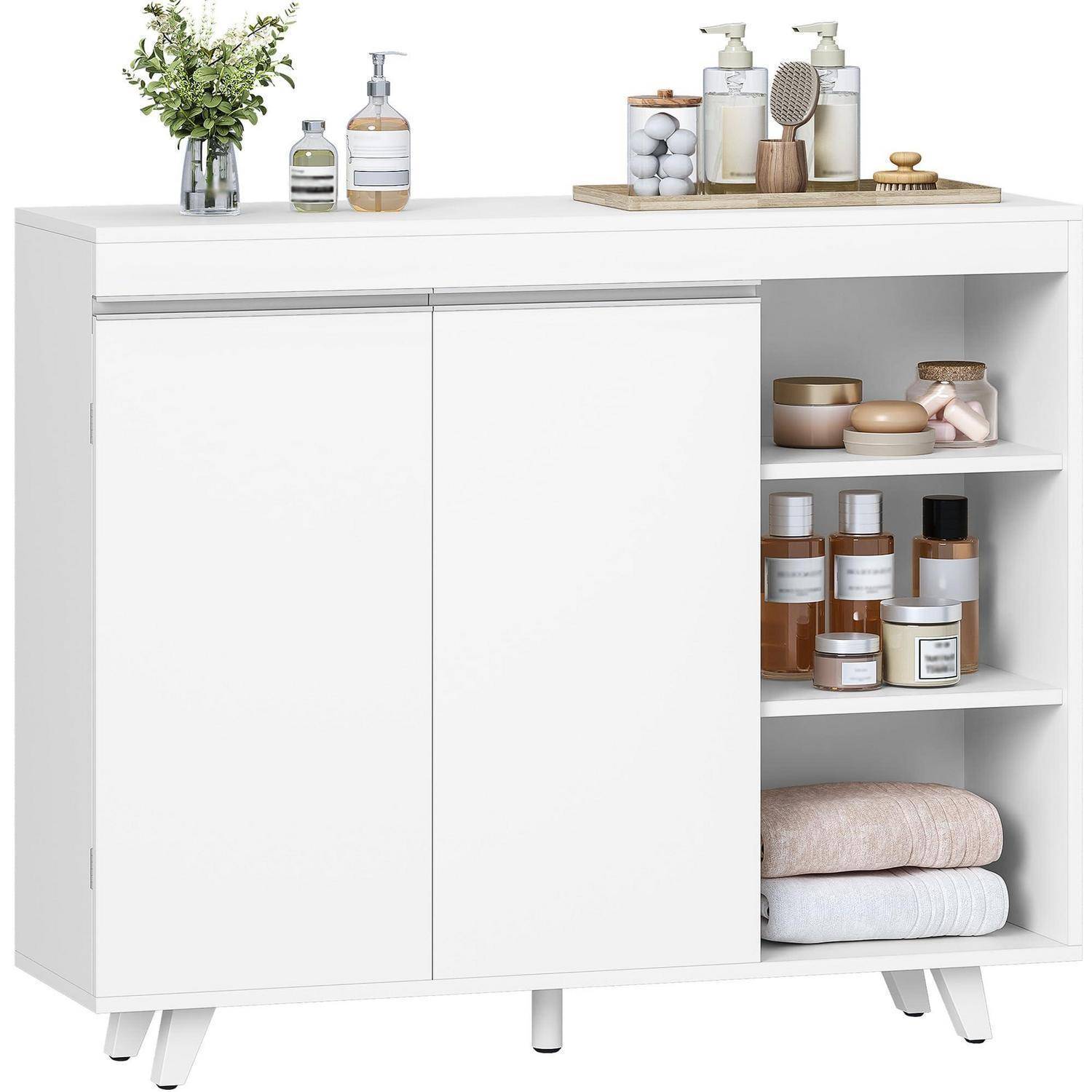Weißer Badezimmerschrank mit zwei Türen und offenen Regalen, auf dem und darin Toilettenartikel, Gläser, Handtücher und Dekorationselemente aufbewahrt sind.