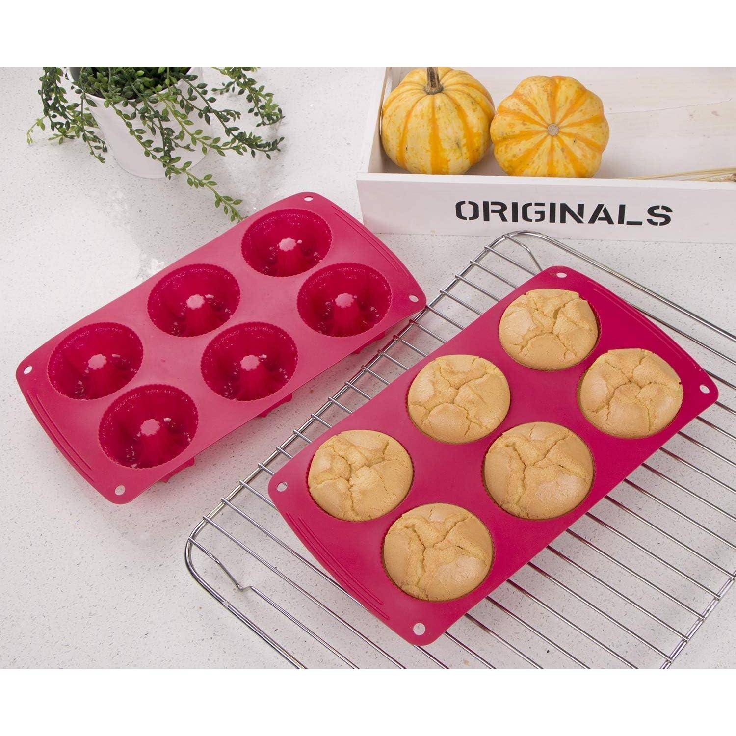 Zwei rosa Silikon-Muffinformen, eine leer und eine mit sechs gebackenen Muffins gefüllt, ruhen auf einem Kühlgitter mit Kürbissen und einer Pflanze im Hintergrund.