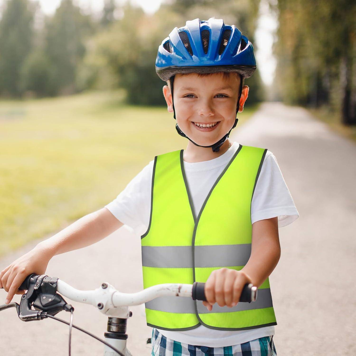 Ein lächelndes Kind trägt einen blauen Fahrradhelm und eine neonorange Sicherheitsweste und fährt auf einem Fahrrad auf einem Weg im Freien.