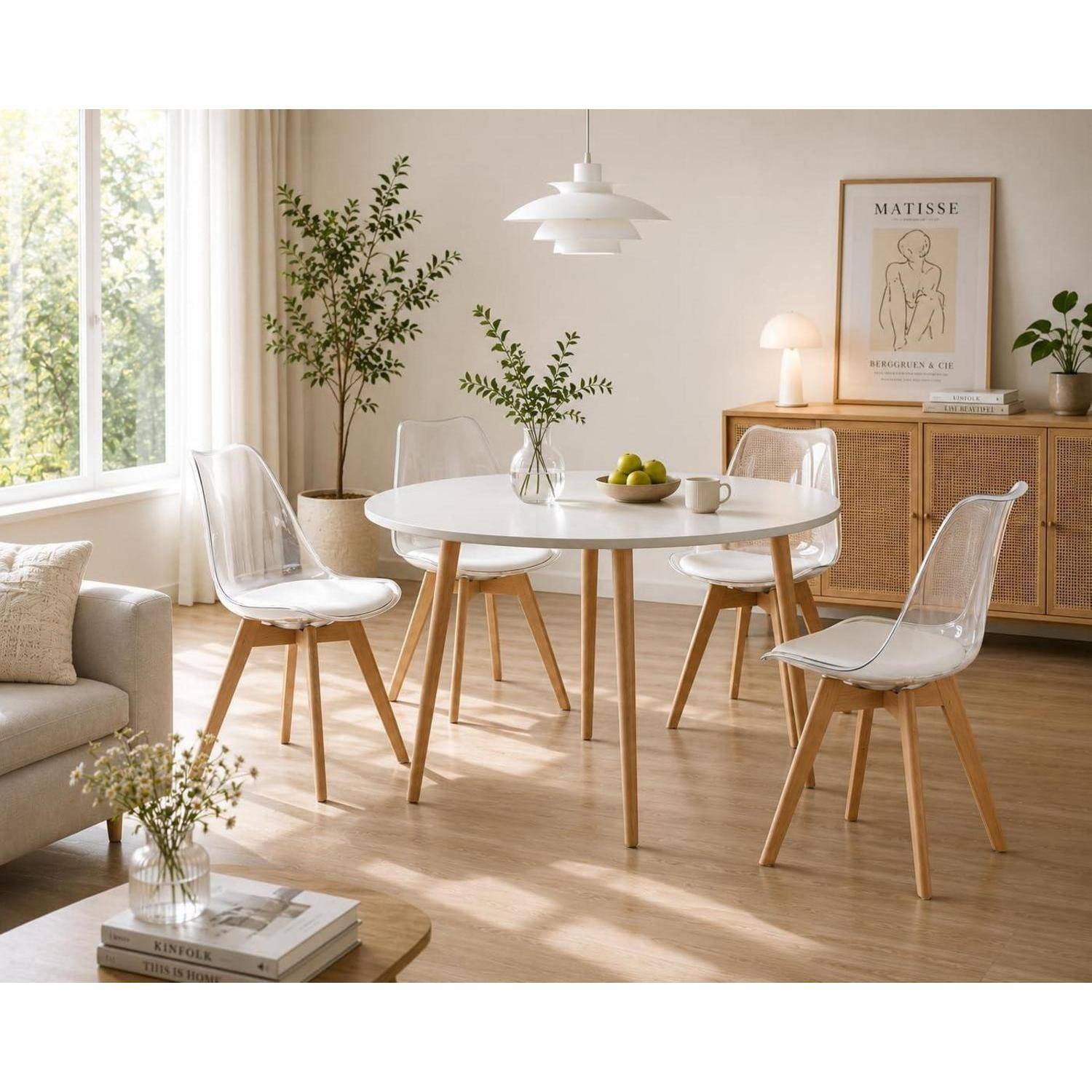 Helles modernes Esszimmer mit einem runden weißen Tisch, transparenten Stühlen, einem Holzschrank und Pflanzen neben einem sonnigen Fenster.