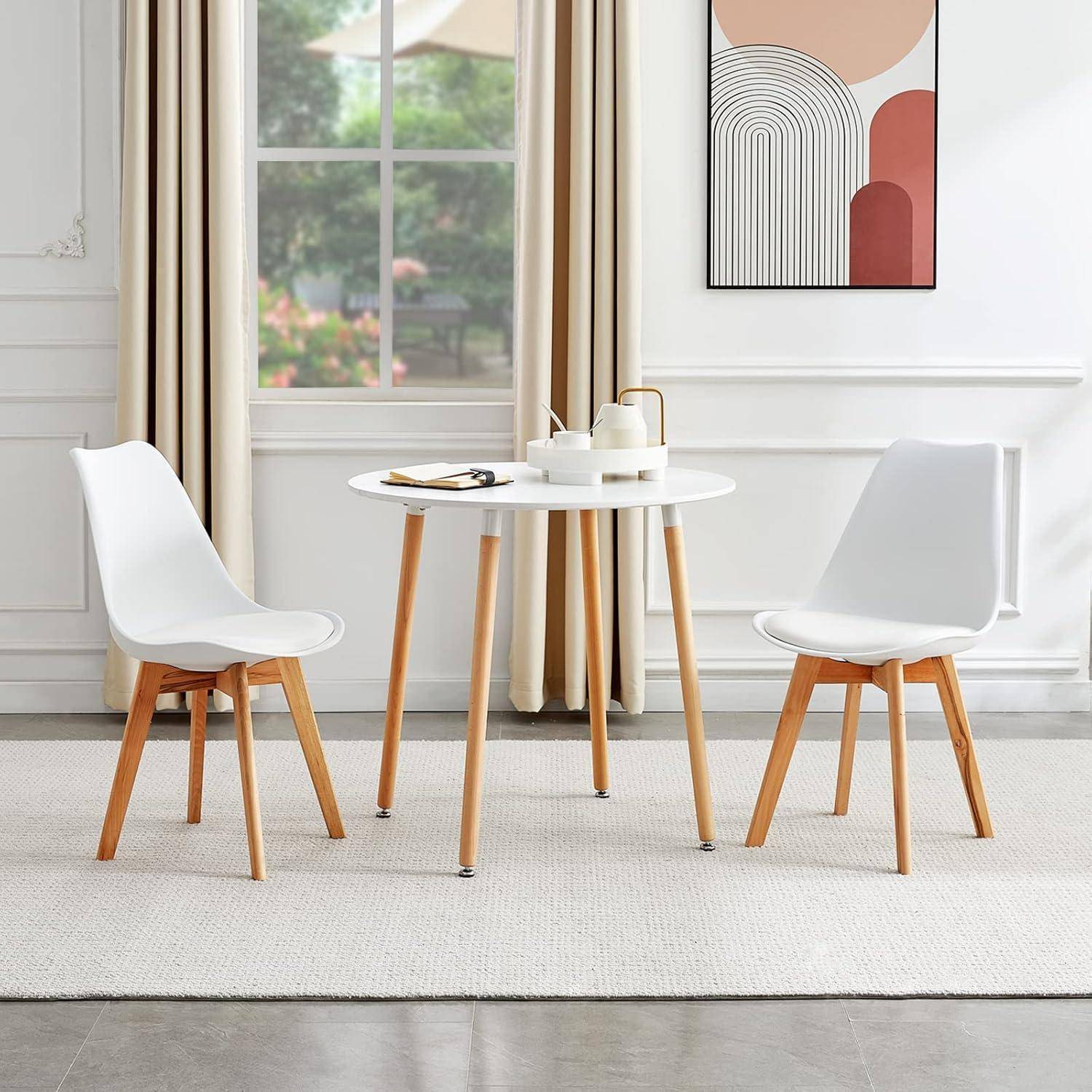 Moderne Essnische mit zwei weißen Stühlen um einen kleinen runden Tisch, eingebettet in einen hellen Raum mit Fenster und Wandkunst.