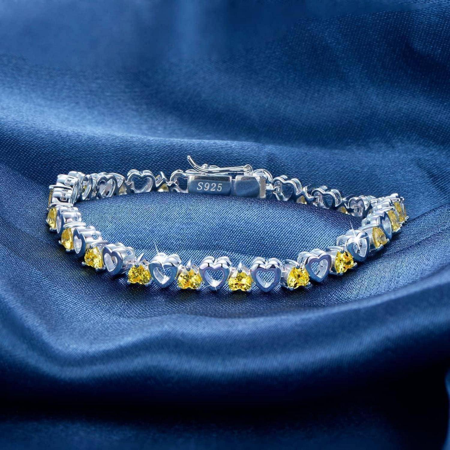 Silberarmband mit herzförmigen Gliedern und gelben Edelsteinen auf blauem Satin, gestempelt S925.