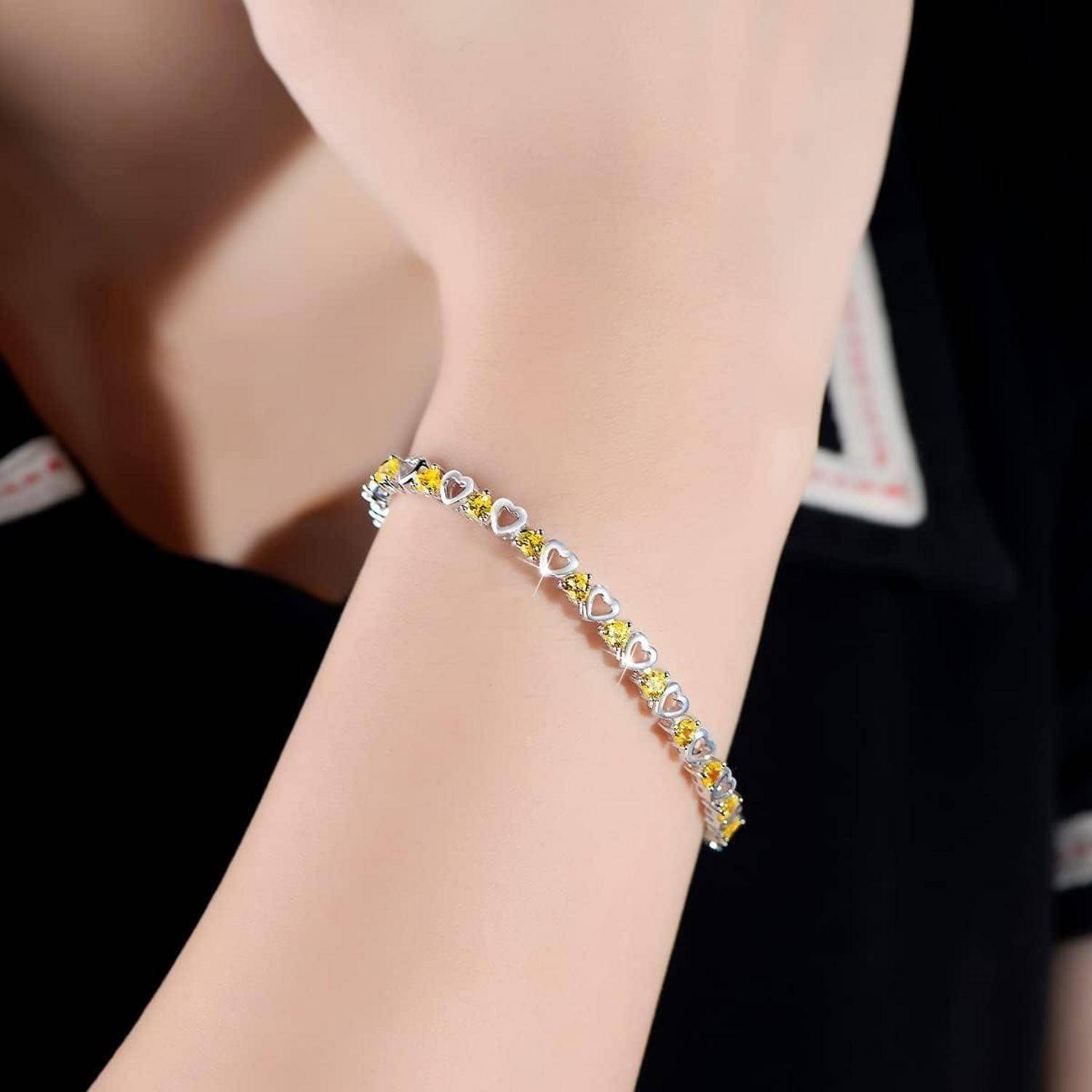 Nahaufnahme eines Handgelenks mit einem zarten silbernen Armband mit kleinen herzförmigen gelben und klaren Steinen.
