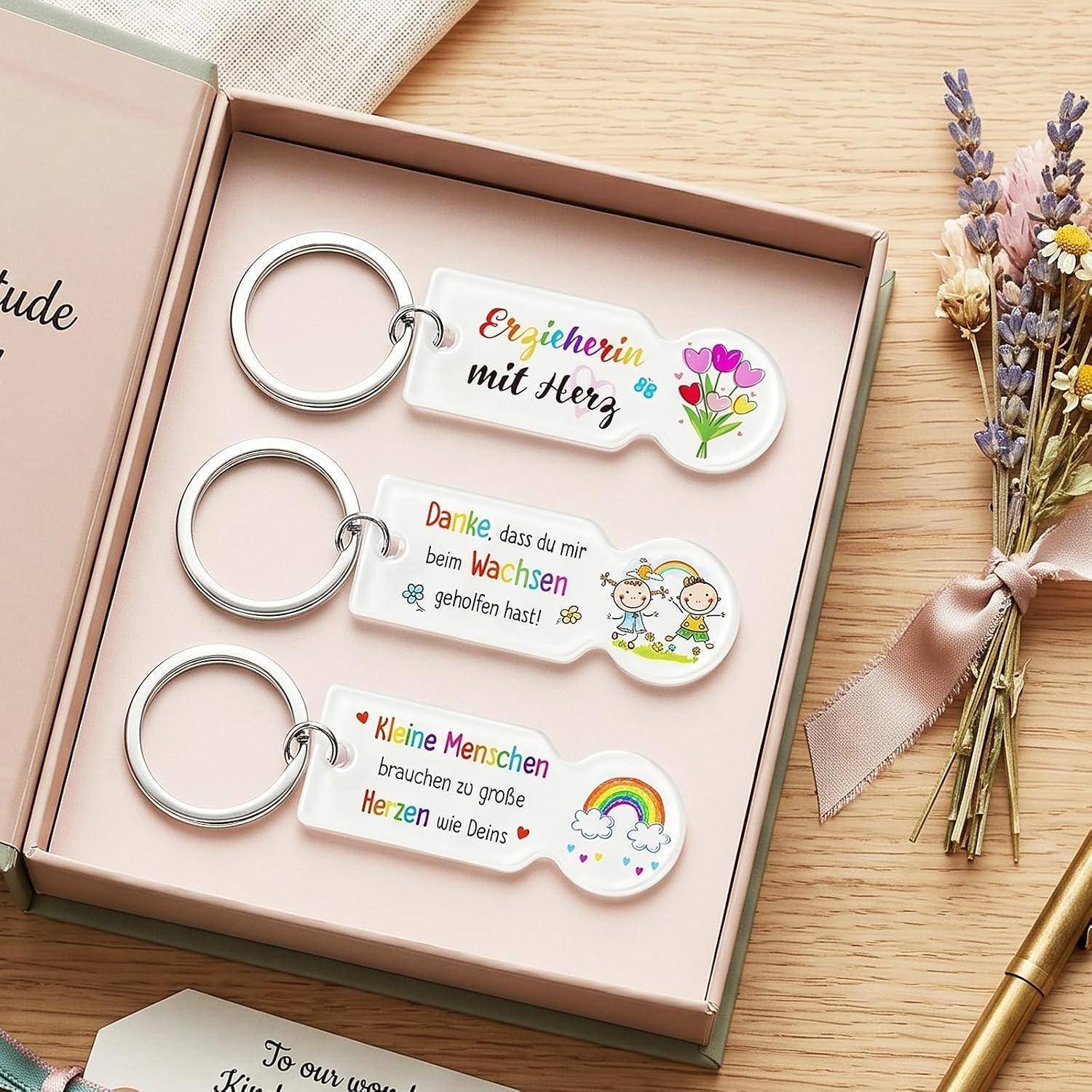 Geschenkbox mit drei gravierten Schlüsselanhängern auf Deutsch: „Erzieherin mit Herz", „Danke, dass du mir beim Wachsen geholfen hast!"" und „Kleine Menschen brauchen zu große Herzen wie Deins"
