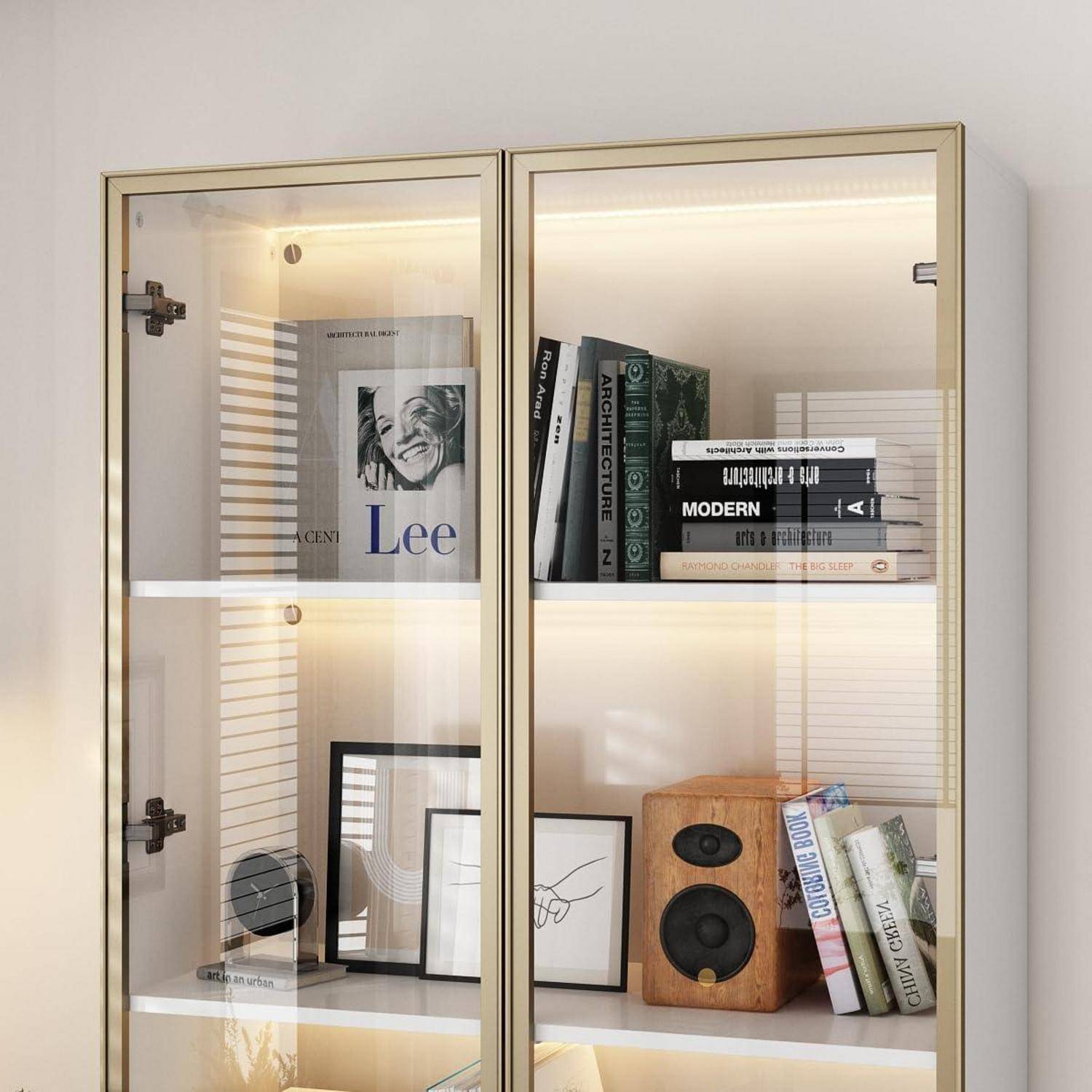 Glaskastenschrank mit Büchern, gerahmter Kunst und einem Holzlautsprecher auf beleuchteten Regalen.