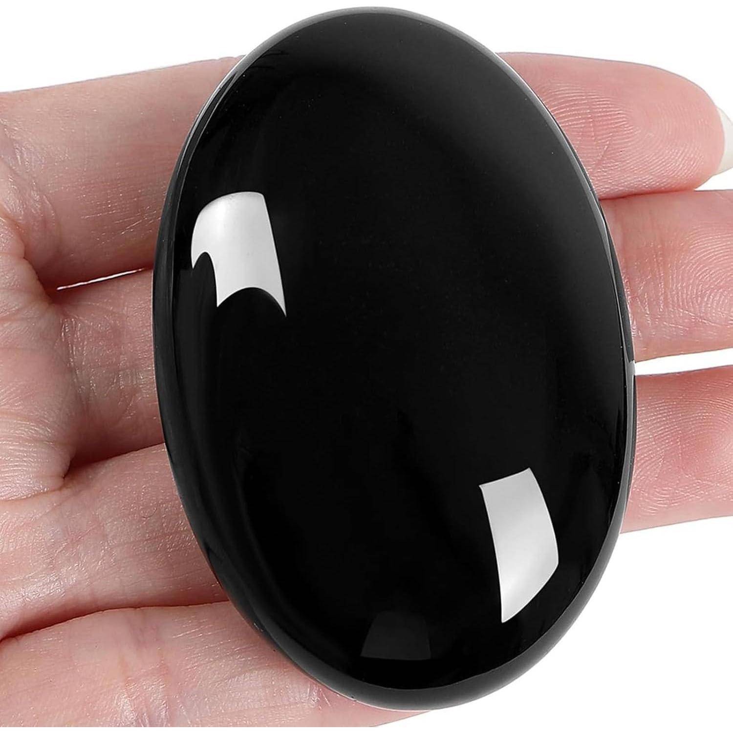 Eine Hand, die einen polierten schwarzen ovalen Edelstein-Cabochon mit einer glänzenden, reflektierenden Oberfläche hält.
