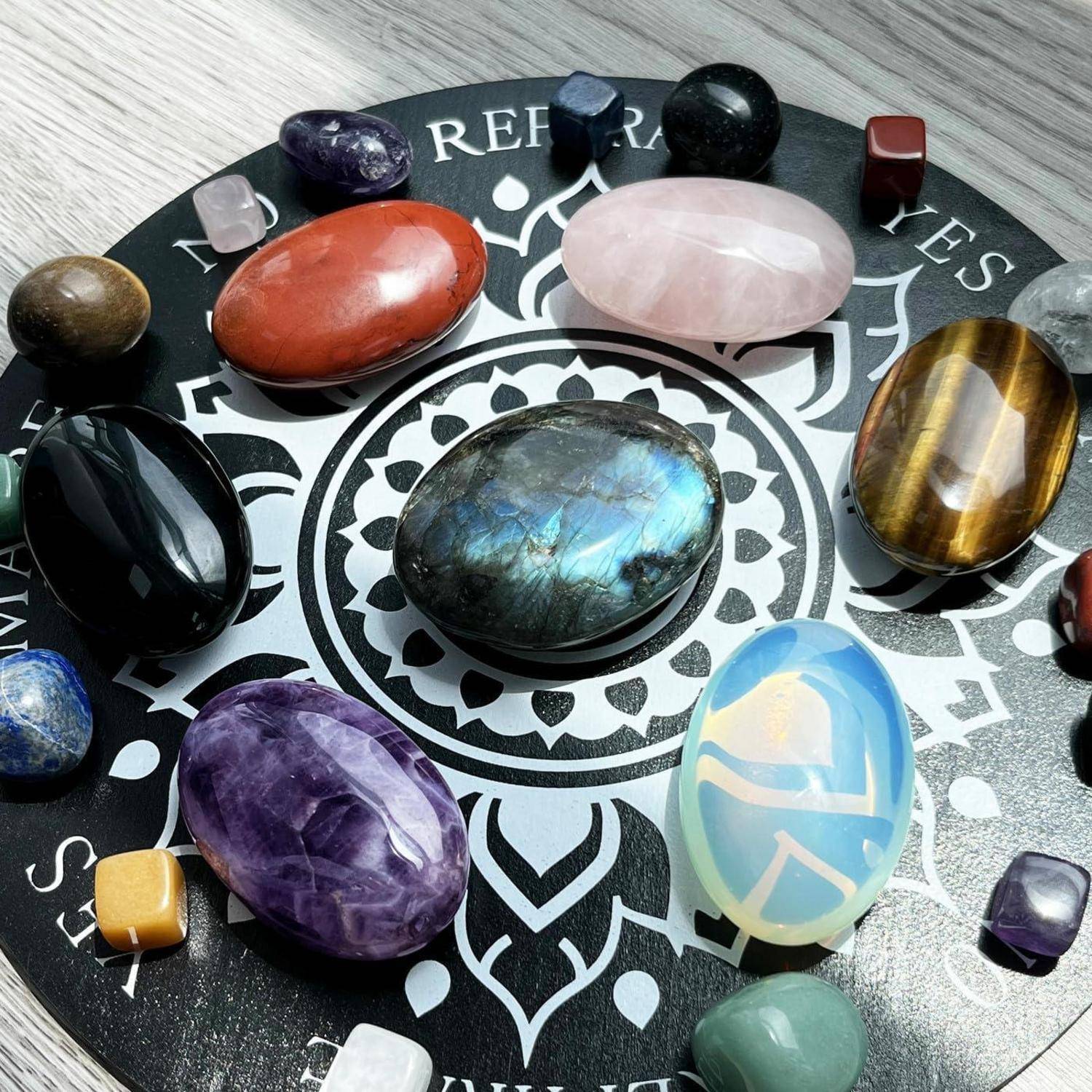 Bunte polierte Edelsteine in einem Kreis auf einem schwarzen Mandala-ähnlichen Brett angeordnet, beschriftet mit Tierkreisnamen, mit einem großen schillernden Stein in der Mitte.