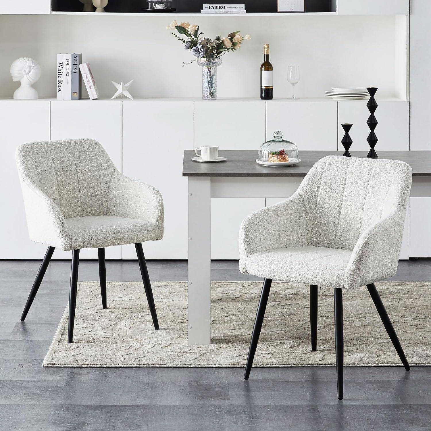 Moderner Essbereich mit zwei weiß gepolsterten Stühlen um einen kleinen Tisch, eingerichtet in einem hellen minimalistischen Raum mit einem Sideboard und Dekoration.