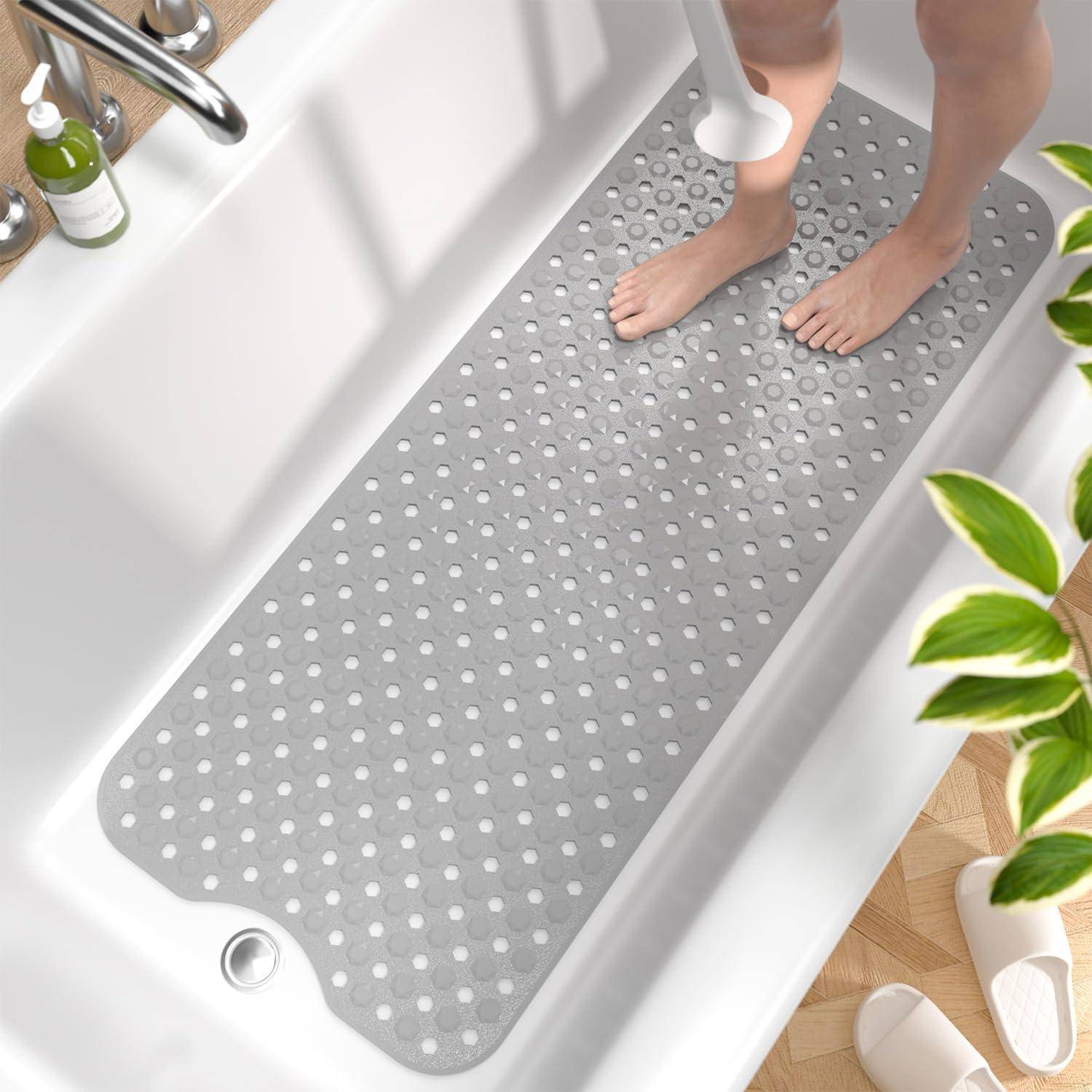 Nackte Füße in einer Badewanne, die auf einer grauen rutschfesten Badewannenmatte mit Saugnapfhaltern stehen, werden von einem tragbaren Handbrausekopf abgespült.