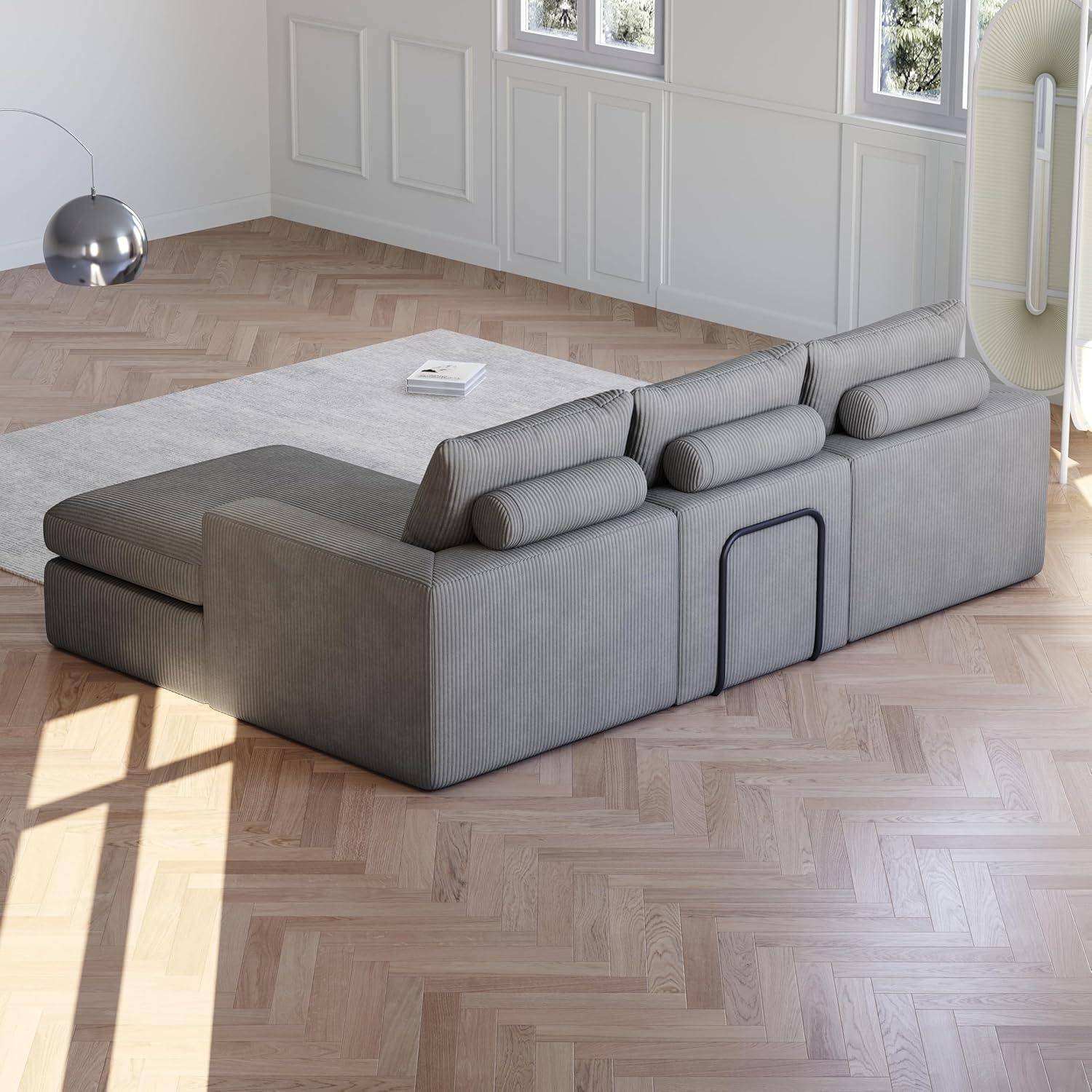 Modernes graues modulares Ecksofa mit eingebauten zylindrischen Kissen in einem hellen Raum mit Fischgrät-Holzboden und weißen Täfelwänden.