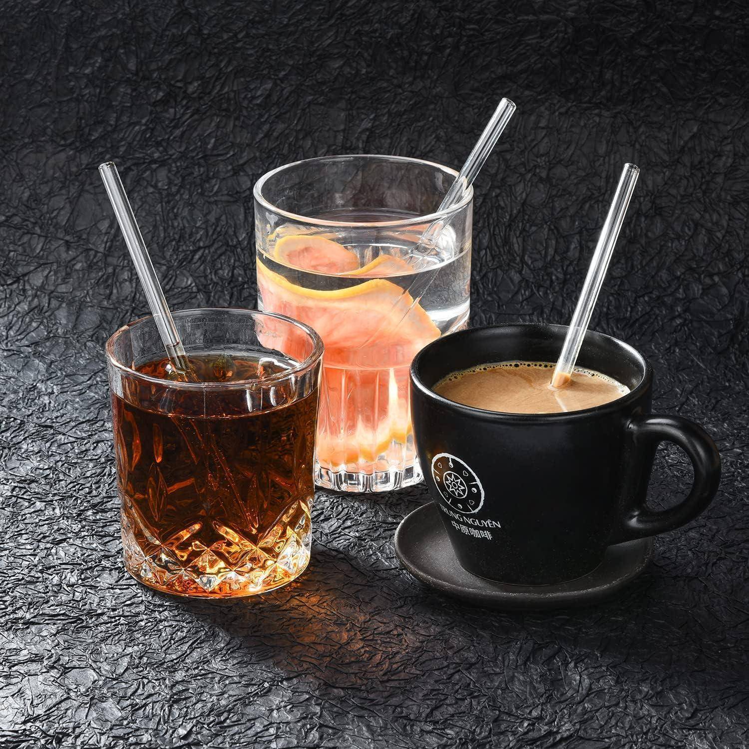 Drei Getränke in Glaswaren und eine schwarze Tasse mit durchsichtigen Strohhalmen, auf einer dunkel strukturierten Oberfläche angeordnet.