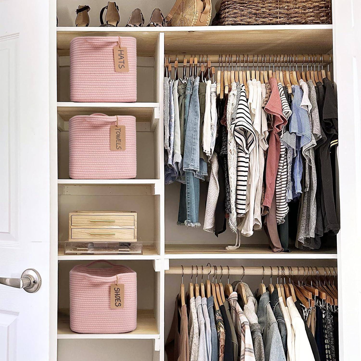 Organisierter Kleiderschrank mit hängender Kleidung, gefalteten Kleidungsstücken und beschrifteten rosa Aufbewahrungsbehältern für Hüte, Handtücher und Schuhe.