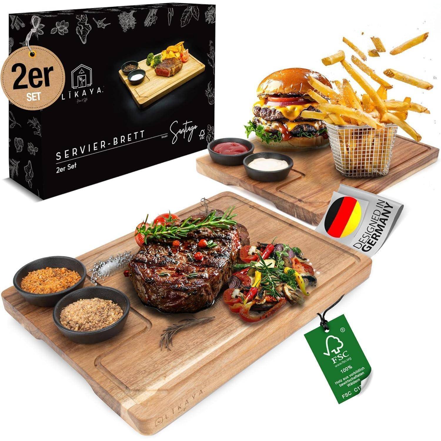 Produktfoto eines 2-teiligen Servierbrett-Sets in einer Schachtel, mit Holzbrettern, auf denen Steak, Burger, Pommes Frites, Saucen und Beilagen angerichtet sind; Etiketten zeigen „Designed in Germany