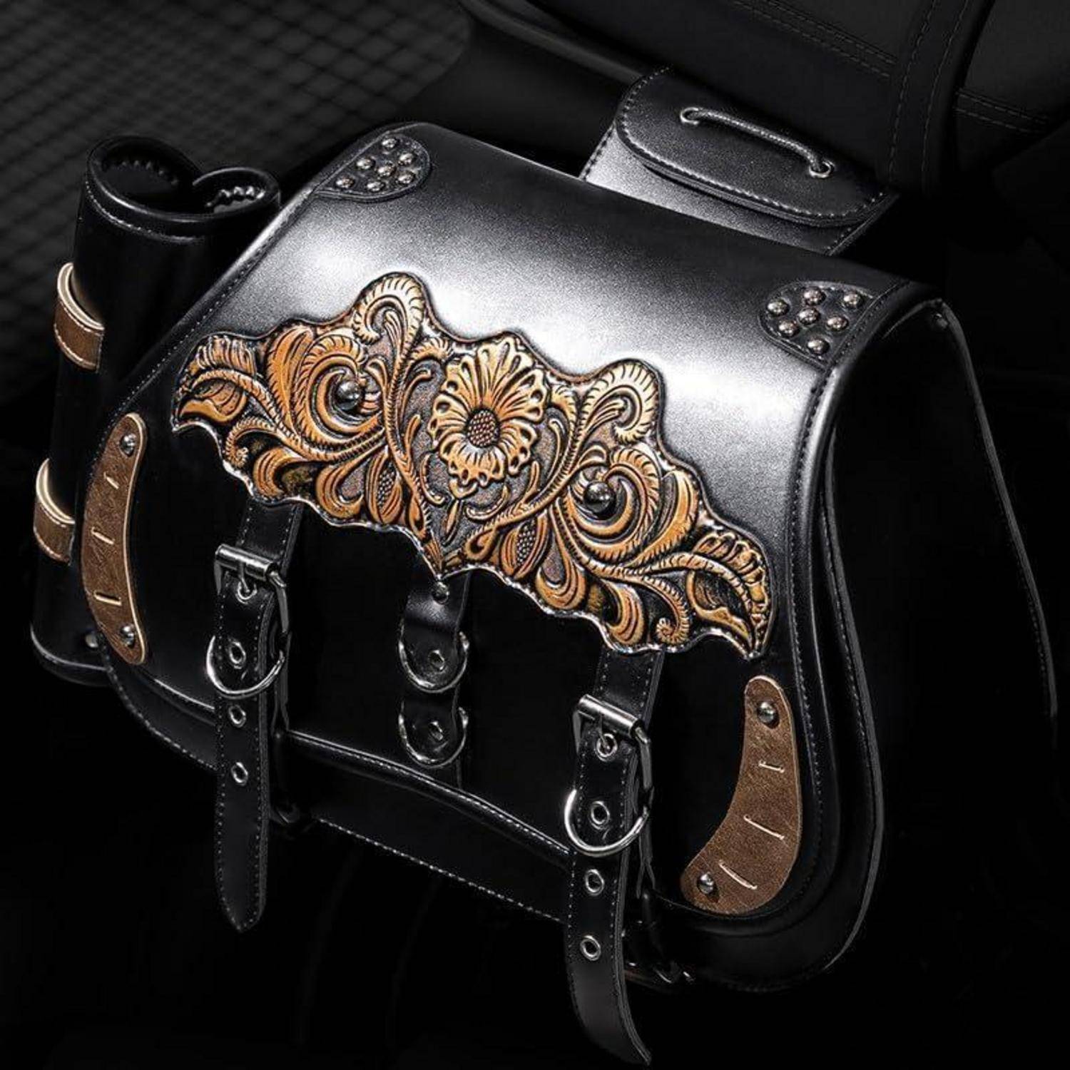 Schwarze Ledersatteltasche mit ornamentaler Blumenschnitzerei und Silbernägeln, vor dunklem Hintergrund gezeigt.