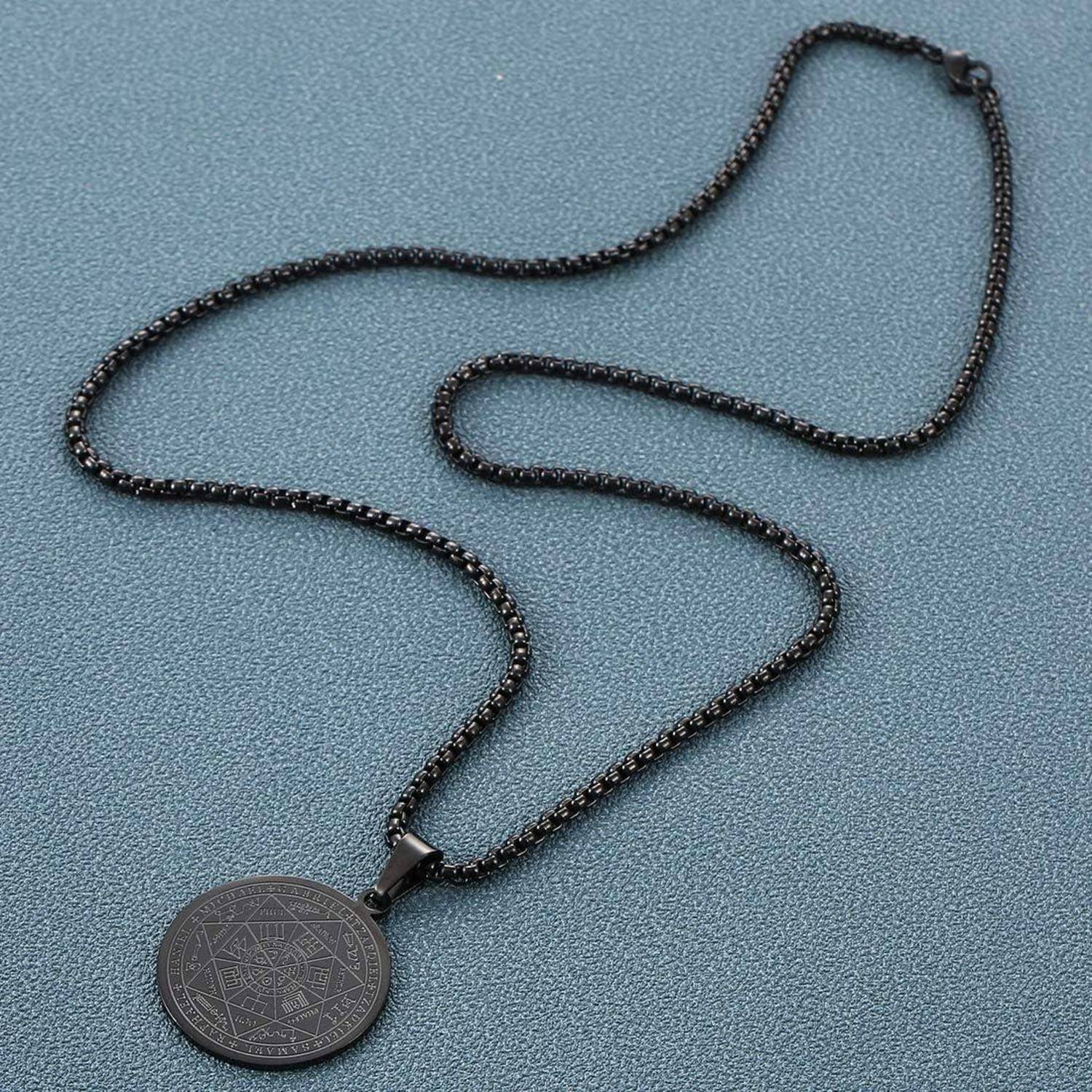Schwarze Perlenkette mit runhänger auf einer blau strukturierten Oberfläche.