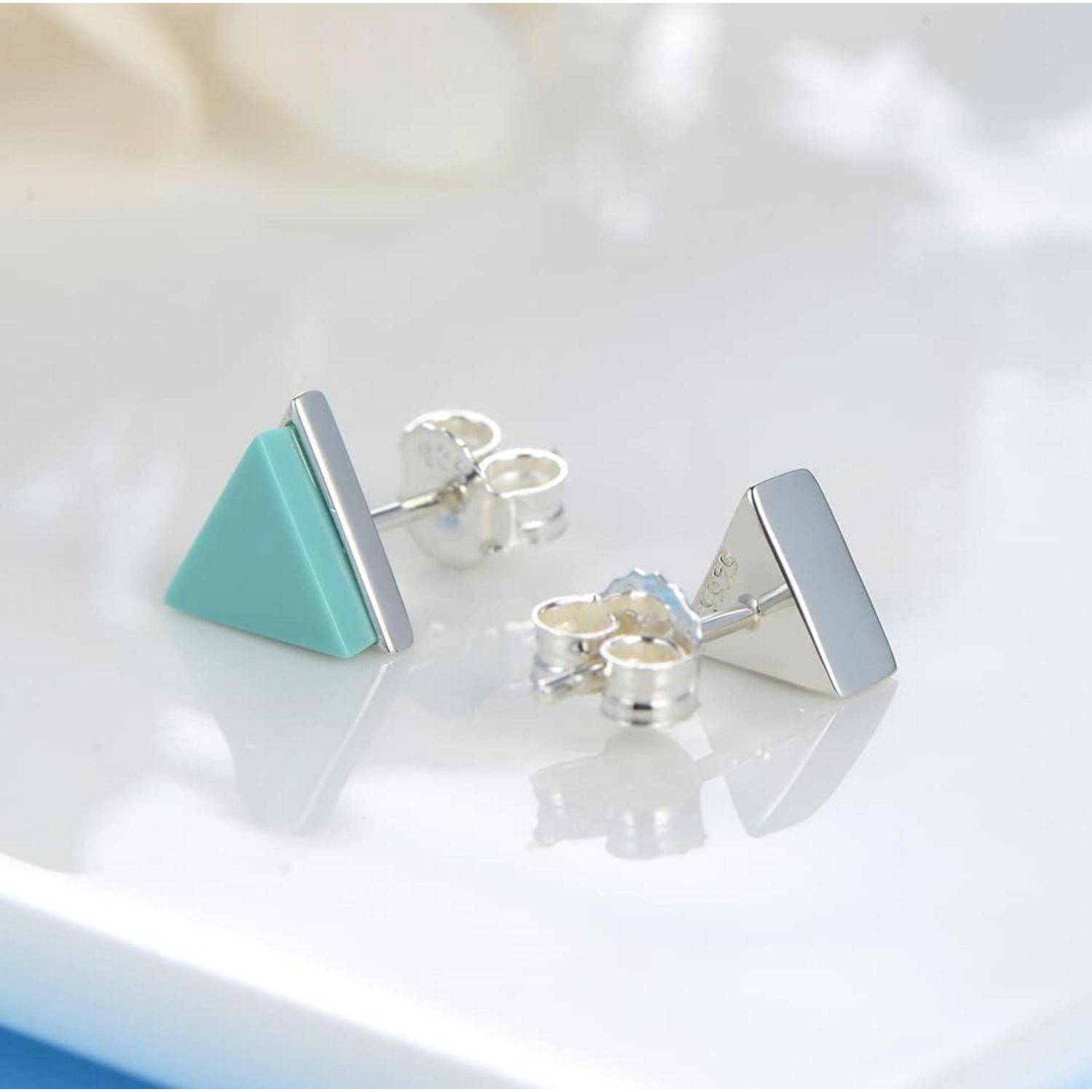 Paar geometrischer Stecker-Ohrringe, ein türkisfarbenes Dreieck und ein silbernes Dreieck, auf einer weißen Oberfläche präsentiert.