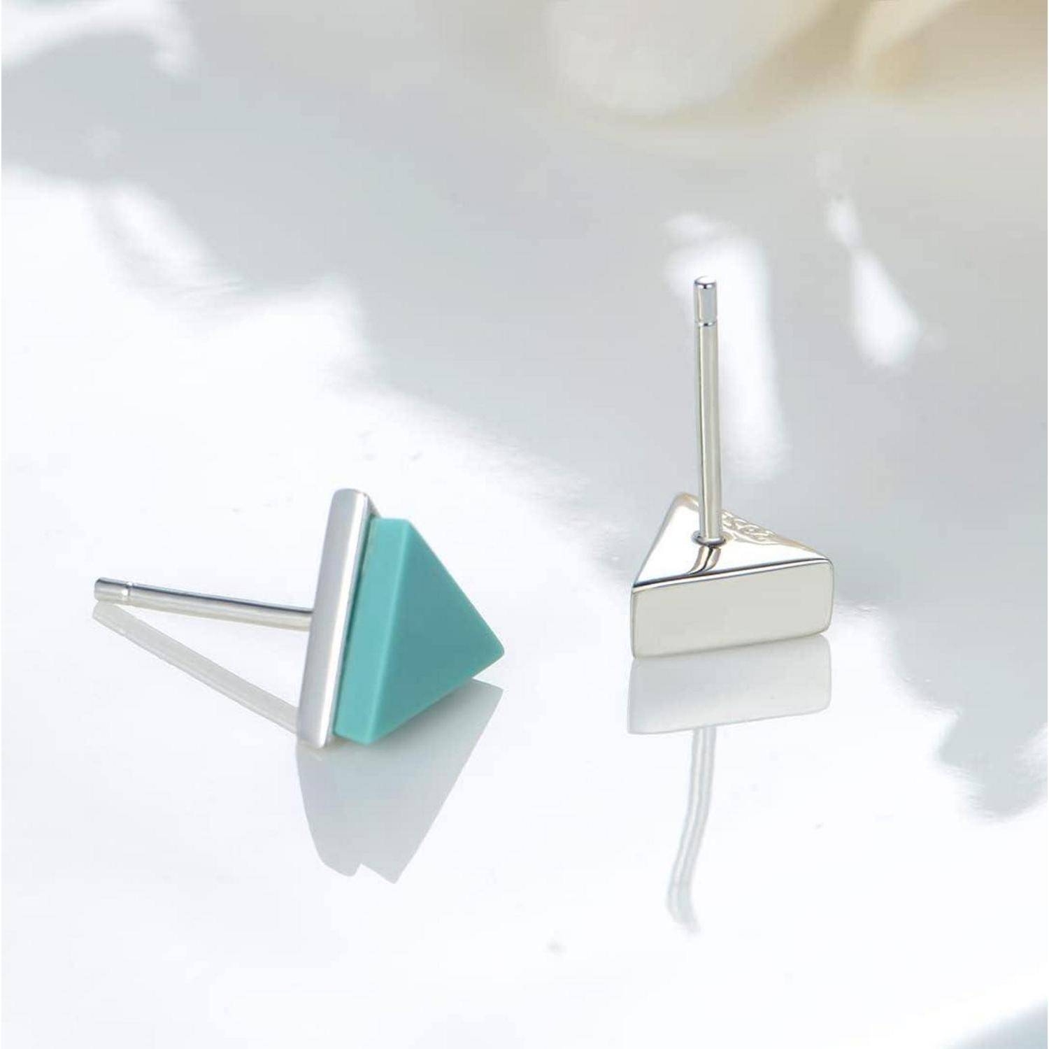 Zwei geometrische Stecker-Ohrringe auf einer weißen Oberfläche, ein türkisfarbenes Dreieck und ein silberner dreieckiger Stecker-Ohrring.