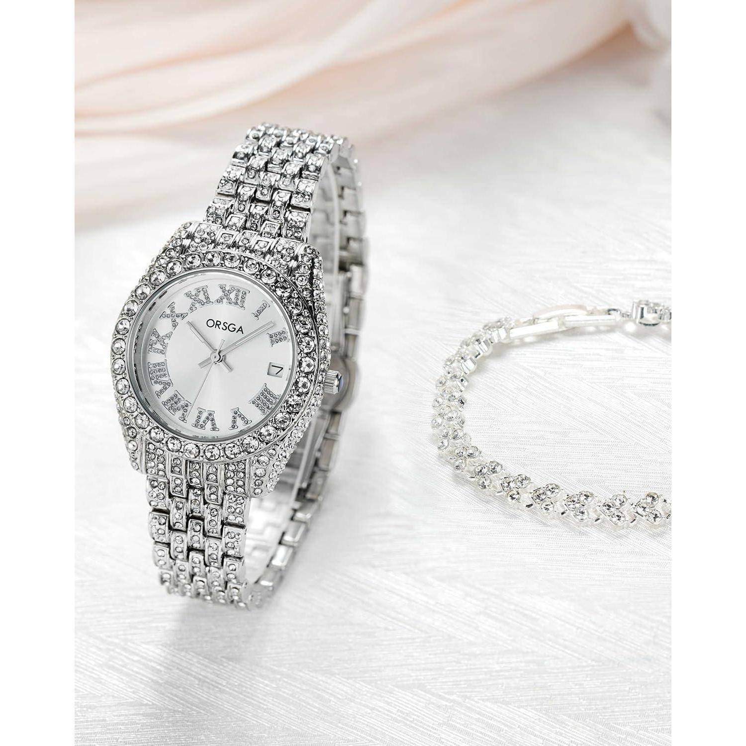 Eine silberne Armbanduhr mit Schmucksteinen und römischen Ziffern wird neben einem passenden Kristallarmband auf einer weißen Oberfläche präsentiert.