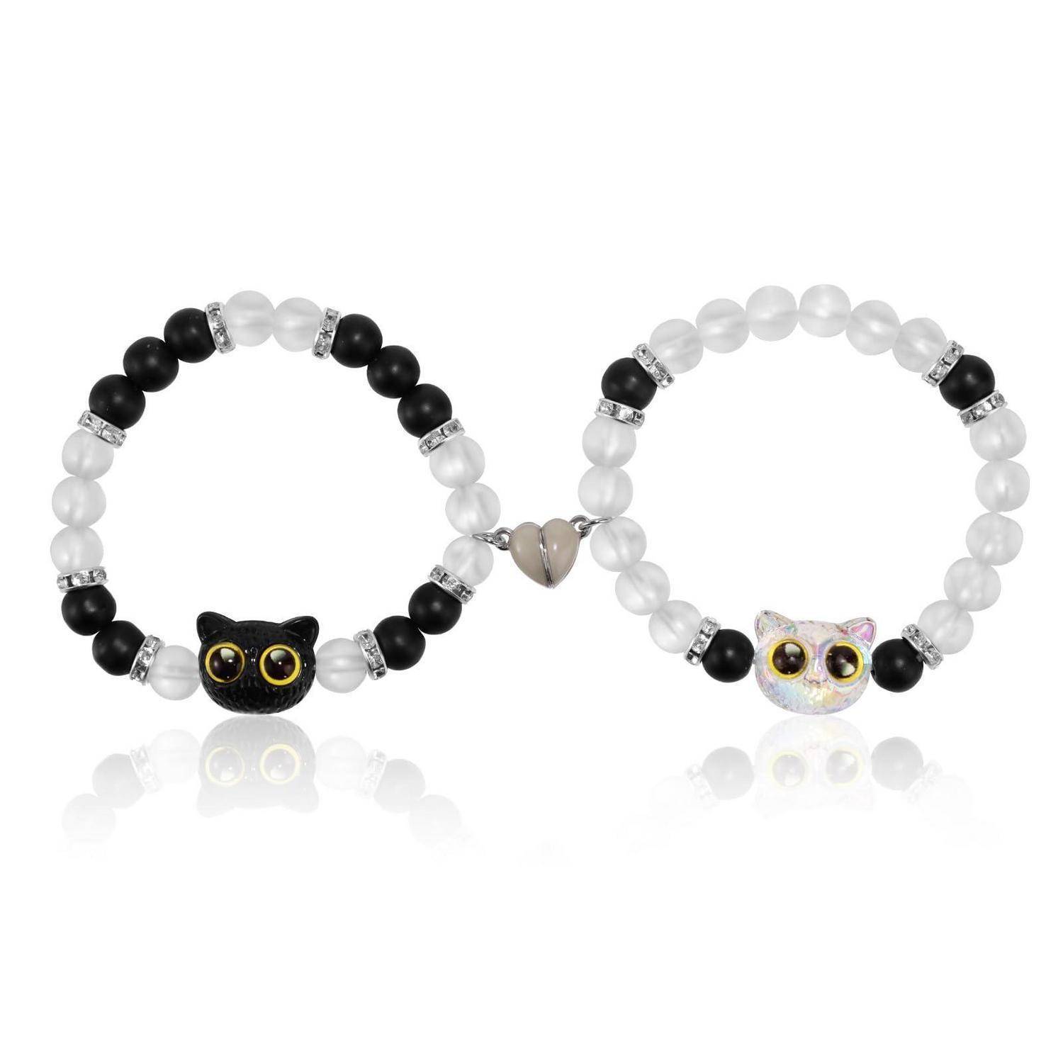 Paar aus Perlen-Katzengesicht-Armbändern, verbunden durch einen kleinen Herzanhänger, eines in Schwarz-Weiß und eines in Weiß mit Regenbogen-Akzenten, auf weißem Hintergrund.