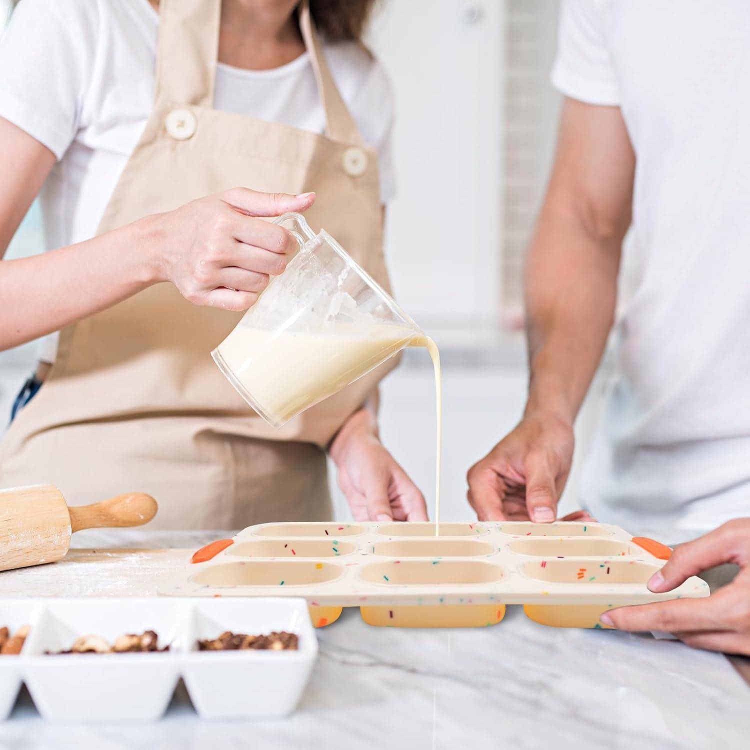 Zwei Menschen gießen Teig in ein antihaftbeschichtetes Muffinblech, während sie in einer hellen Küche stehen, mit Backzutaten und Eierkartons in der Nähe.