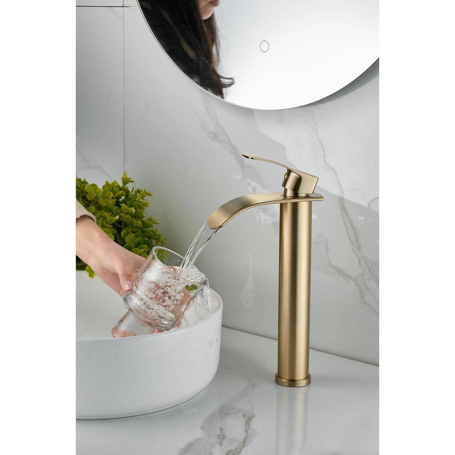 Goldfarbener Wasserhahn füllt ein Glas aus einem weißen Waschbecken, wobei eine Hand einer Person das Glas in einem modernen Marmorbadezimmer hält.