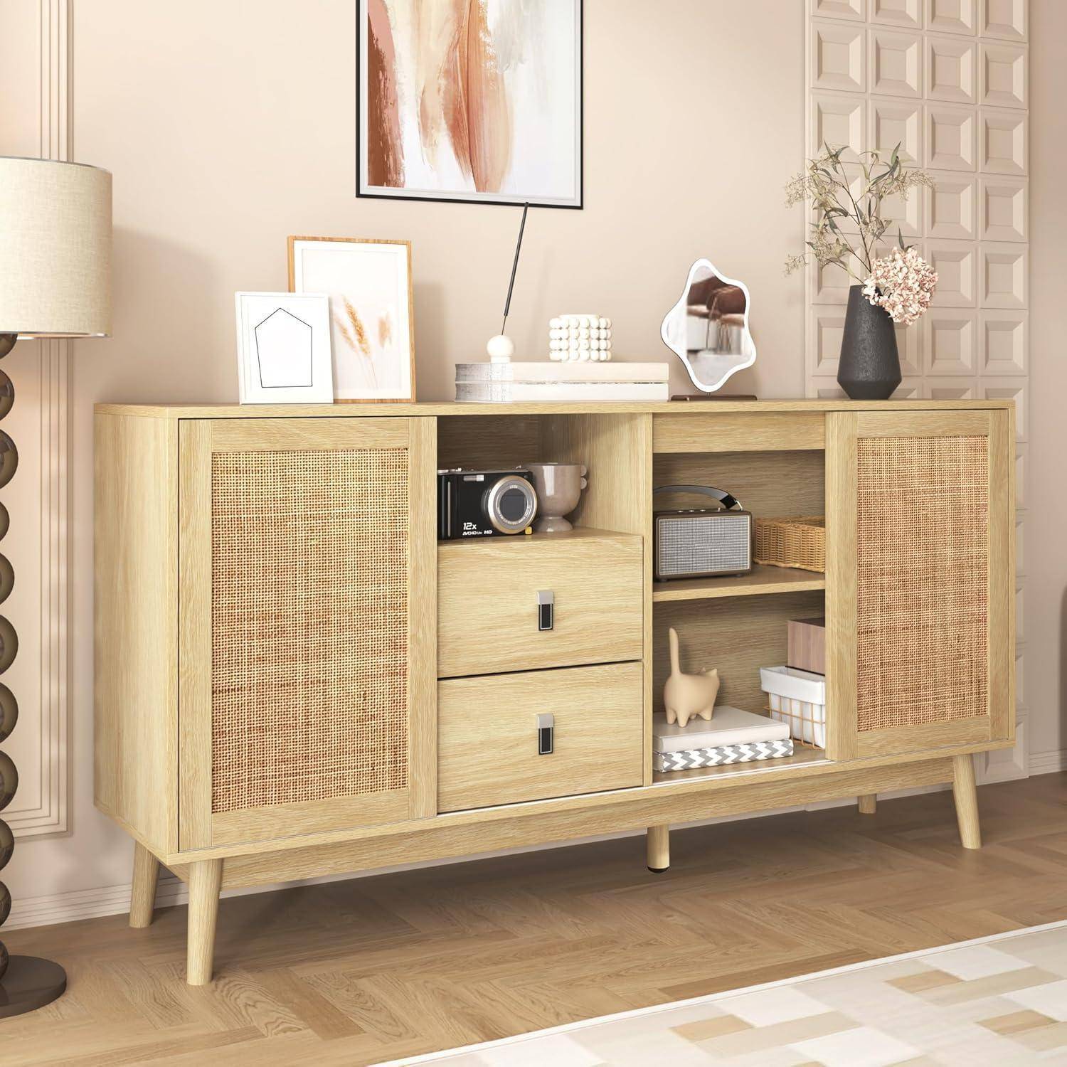 Helles Holz-Sideboard mit geflochtenen Türen, offenen Regalen und Schubladen, dekoriert mit Rahmenbildern, Lampe, Spiegel und Vasen in einem hellen Raum.