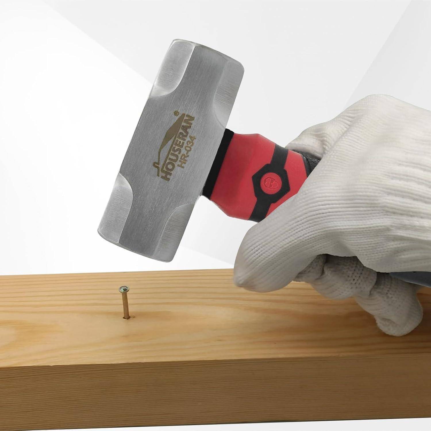 Eine behandschuhte Hand hält einen Hammer über einen teilweise in ein Holzbrett getriebenen Nagel und zeigt eine laufende Schreinerarbeit.