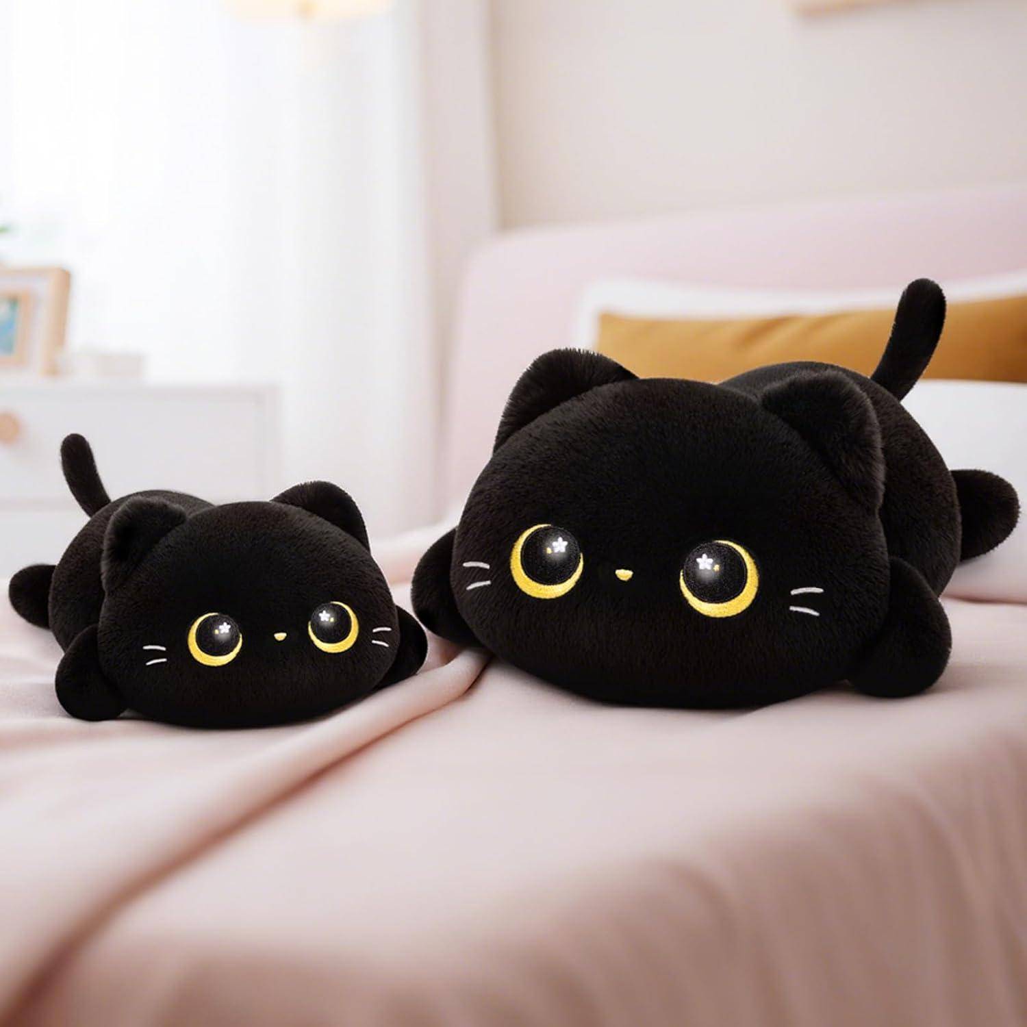 Zwei schwarze Plüschkatzenspielfiguren mit gelben Augen liegen auf einem rosa Bett, eine kleine und eine große, in einer hellen Schlafzimmerumgebung.