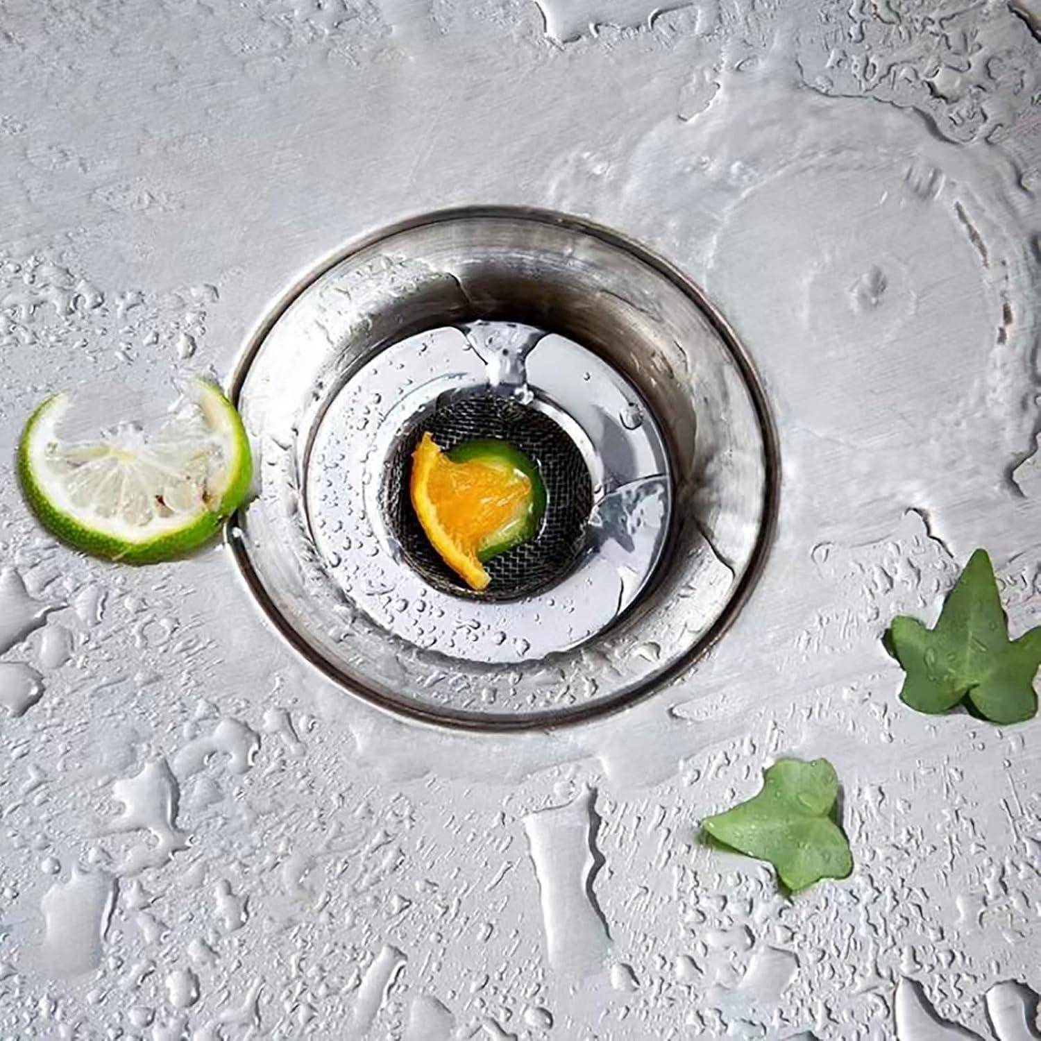 Draufsicht auf einen Küchenspülabfluss mit einer Zitrusschale, die im Sieb steckt, umgeben von Wassertropfen, einer Limettenscheibe und kleinen Blattfetzchen.