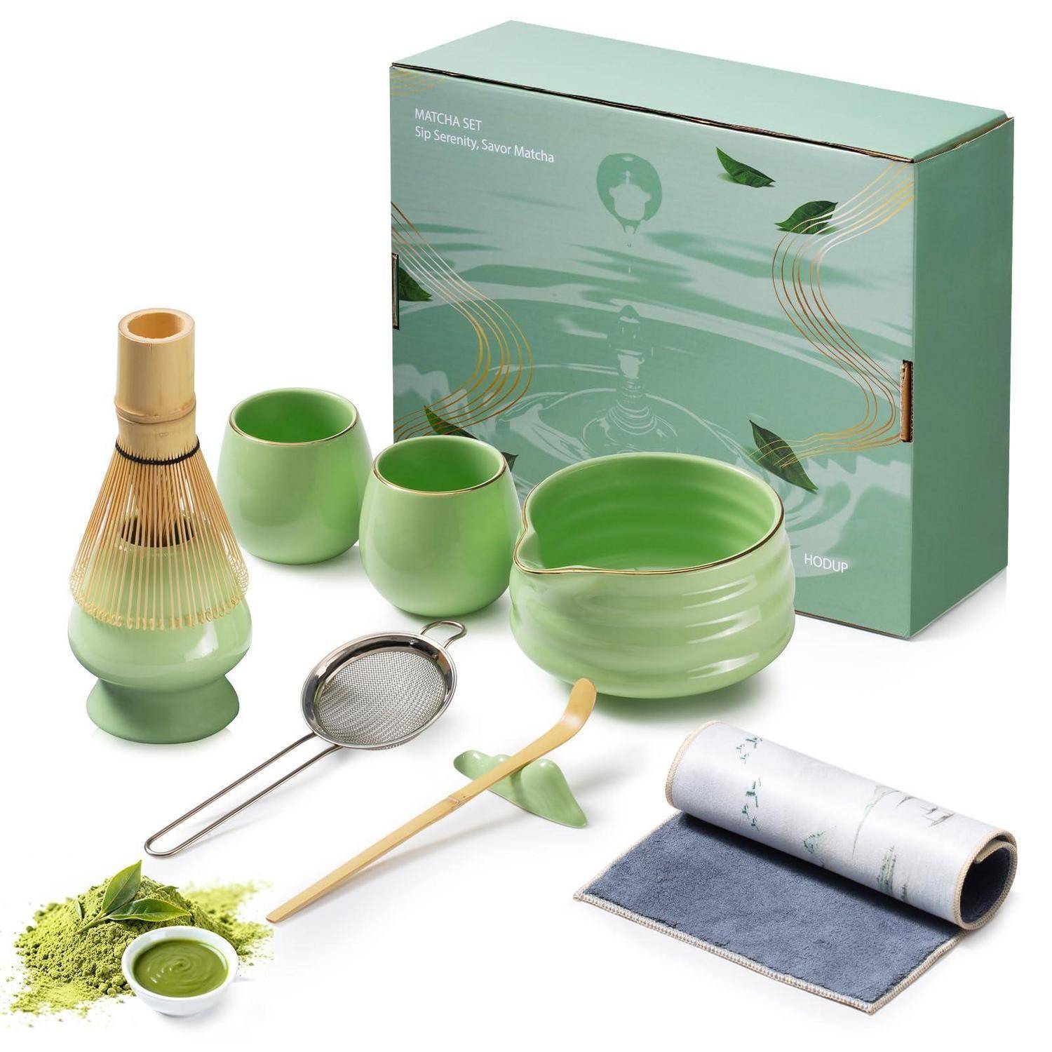Grünes Matcha-Tee-Set mit Schüssel, Tassen, Schneebesen, Löffel, Sieb, Tuch, Pulver und Aufbewahrungsbox auf weißem Hintergrund.