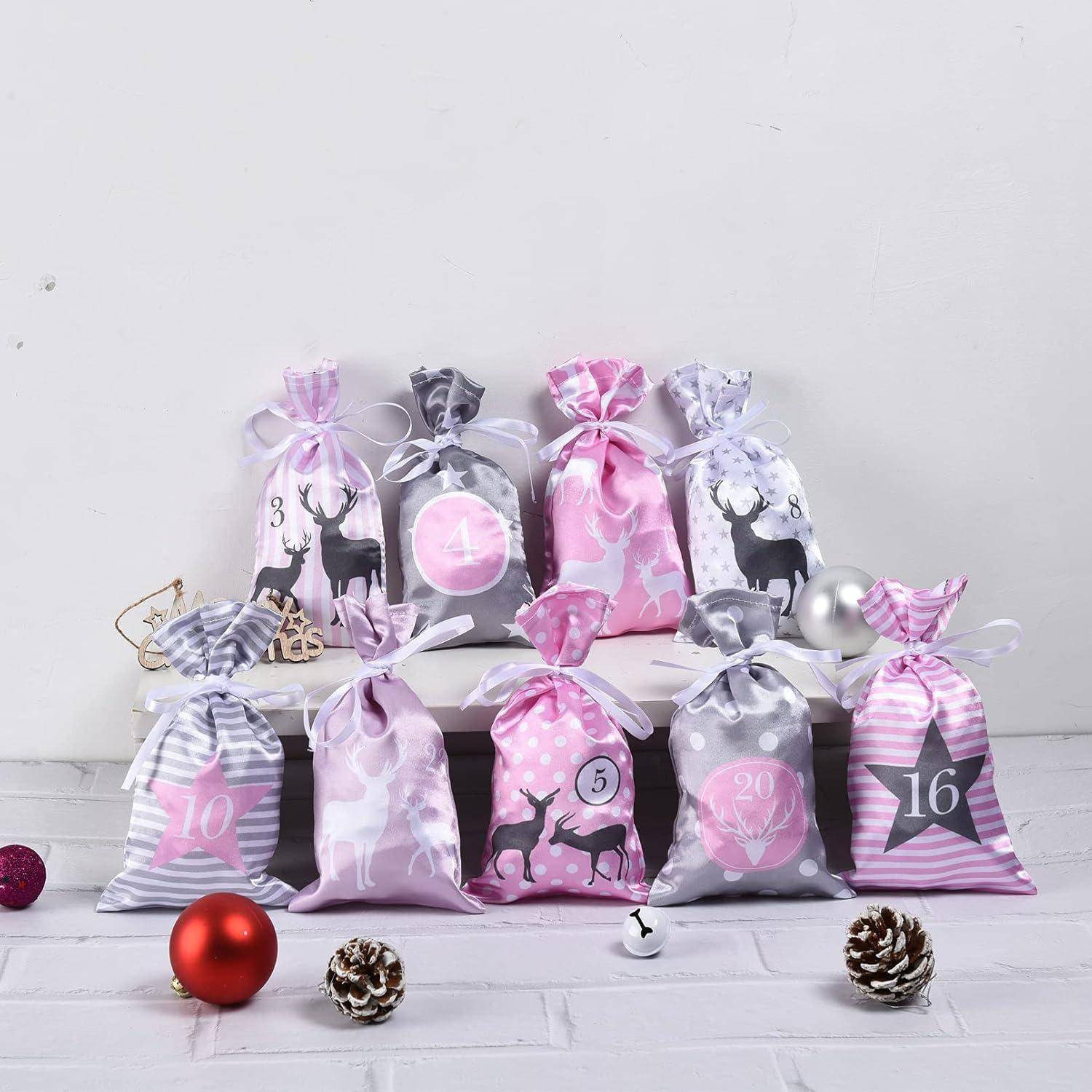 Adventskalender-ähnliche Reihe von rosa und grauen Geschenktaschen mit Kordelzug, nummerierten Etiketten, Hirschdrucken und Schleifenbändern auf einem weißen Regal und Boden.