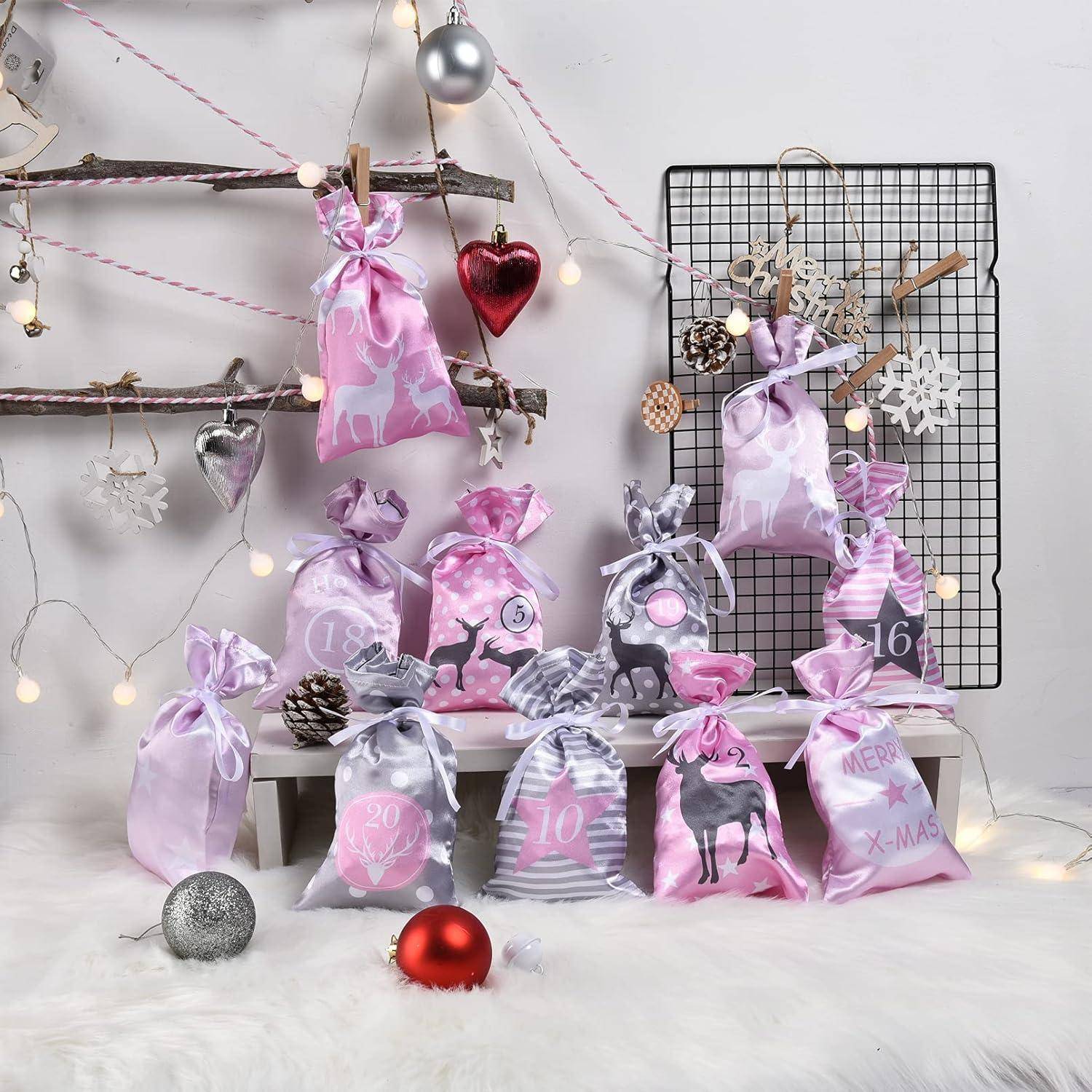 Rosa und graue Weihnachtsgeschenktüten und Ornamente auf einer weißen Pelzoberfläche angeordnet, mit Feenlichtern und einem mit Drahtgitter-Hintergrund dekoriert für die Feiertage.