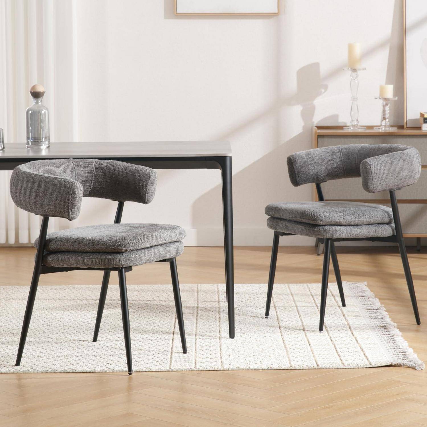 Modernes Esszimmer mit zwei grau gepolsterten Stühlen, einem schwarzen Tisch, hellem Teppich und einer Anrichte in einem hellen minimalistischen Interieur.