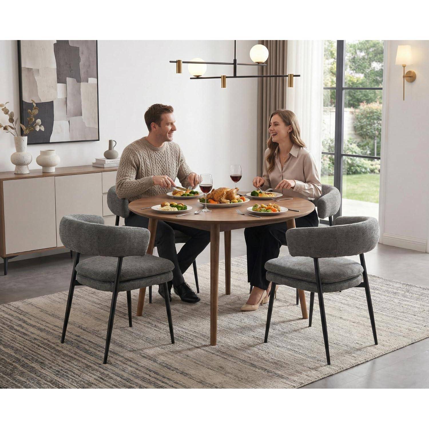 Ein Mann und eine Frau teilen sich eine Mahlzeit an einem runden Esstisch in einem hellen modernen Esszimmer mit gepolsterten Stühlen und einem großen Fenster.