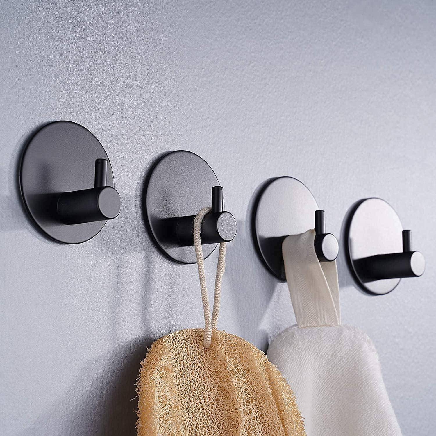 Vier an der Wand montierte runde Haken an einer hellen Wand, die einen Badeschwamm und zwei hängende Handtücher halten, zeigen eine Badezimmer-Aufbewahrungslösung.