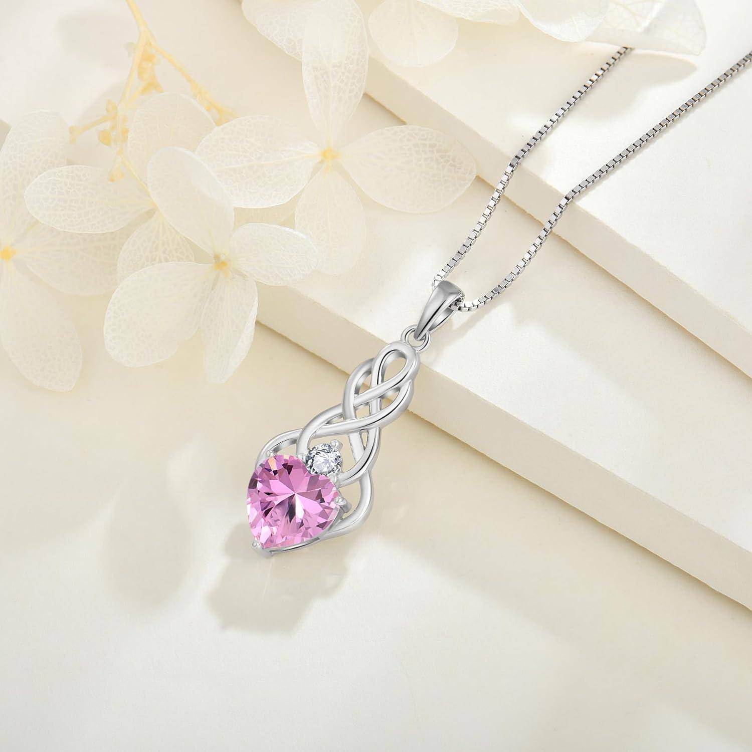 Silberkette mit Anhänger mit verflochtener Herzform und rosa Edelstein, präsentiert auf einem cremefarbenen Blumenhintergrund.