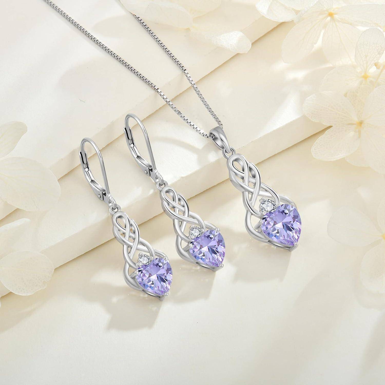 Silberne herzförmige Edelsteinkette und passende Ohrringe mit violetten Steinen auf hellblumigem Hintergrund.