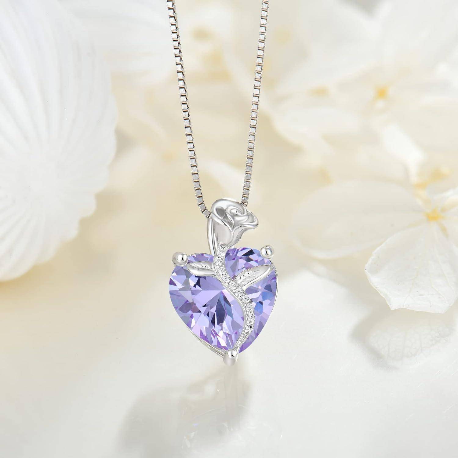 Silbernes herzförmiges Anhängerkettchen mit einem violetten Edelstein und kleinen klaren Steinen an einer feinen Kette, gezeigt vor einem weichen Blumenhintergrund.
