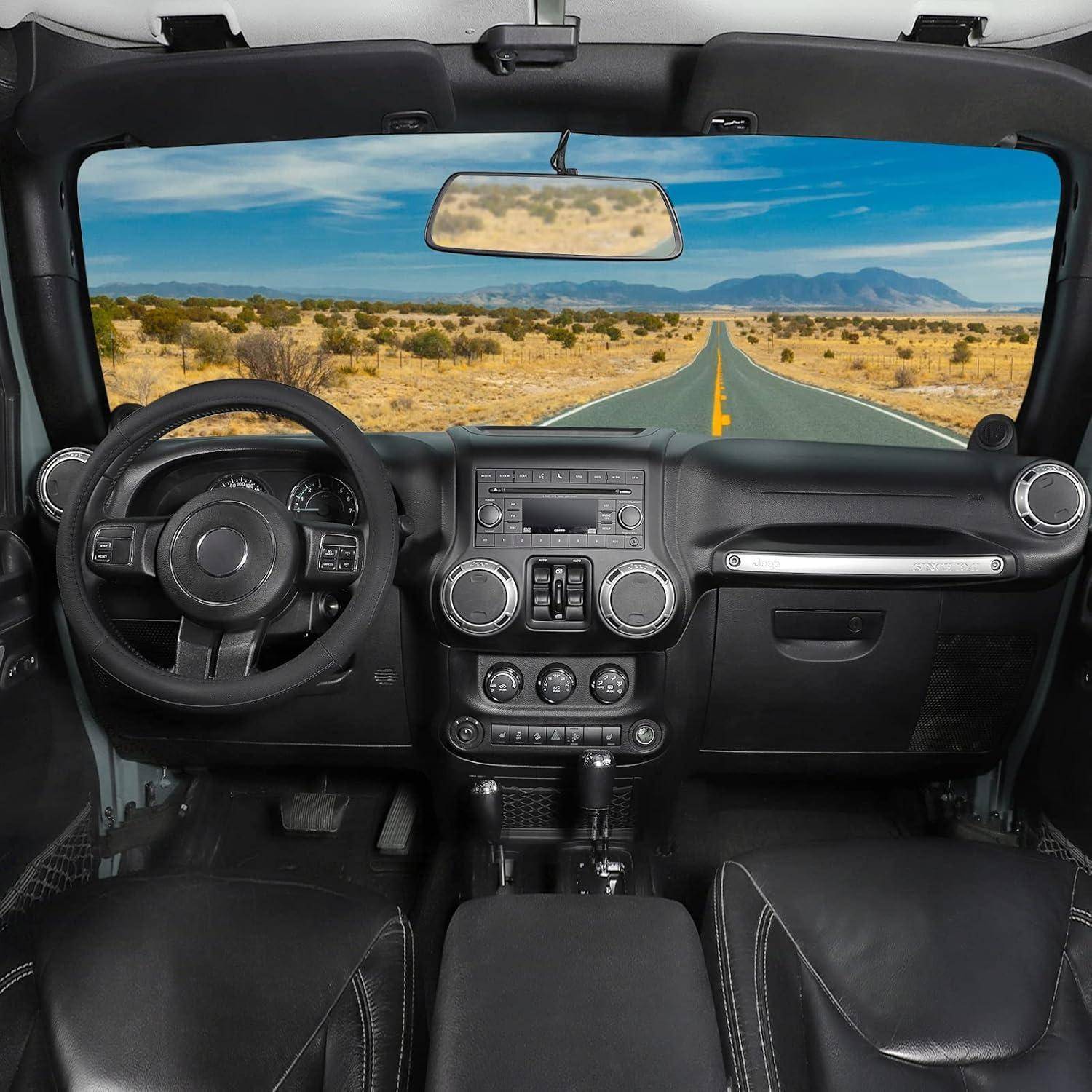 Innenraum eines Jeep-ähnlichen Fahrzeugs mit Armaturenbrett, Lenkrad und Sitzen, wobei eine gerade Wüstenstraße durch die Windschutzscheibe sichtbar ist.