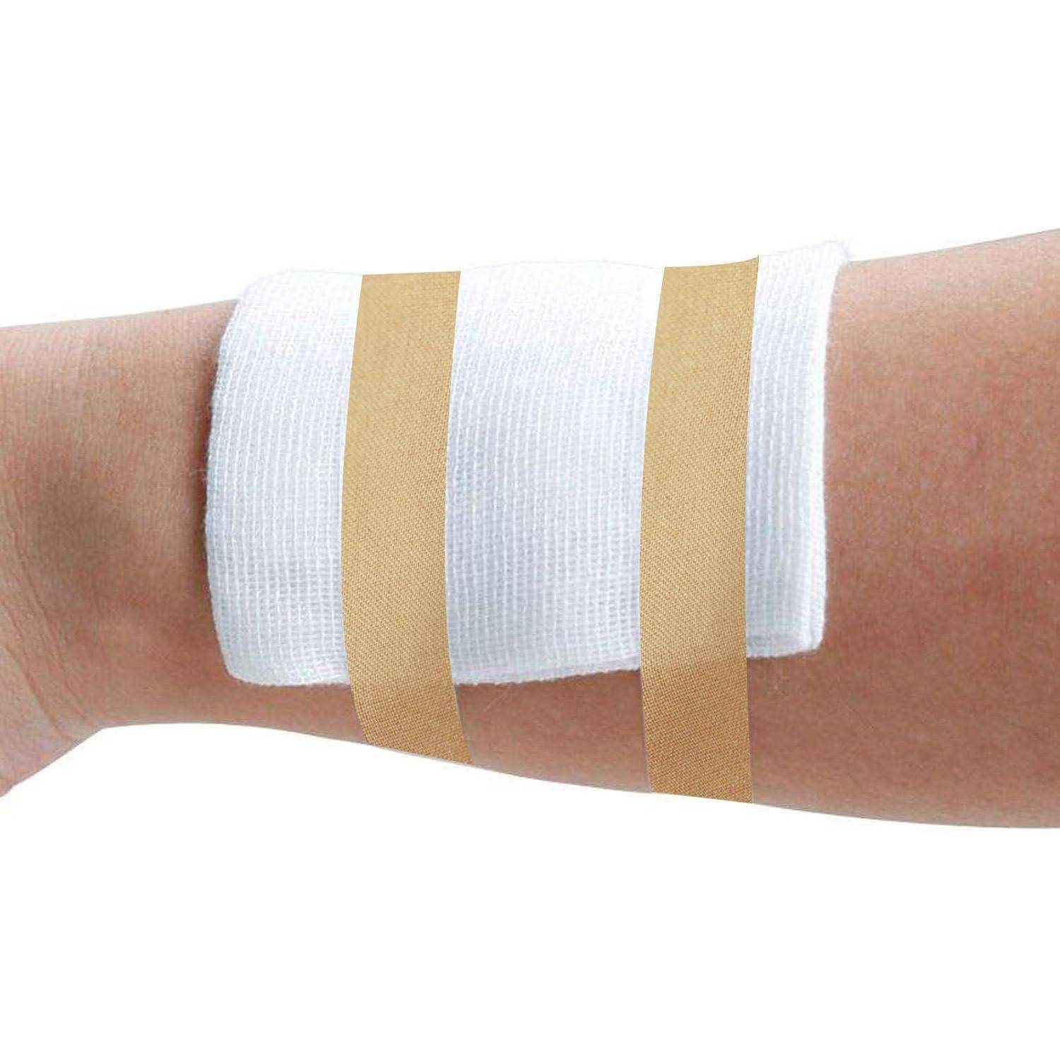 Nahaufnahme eines Unterarms mit einem weißen Mullverband, der durch zwei beige Heftpflaster befestigt ist.