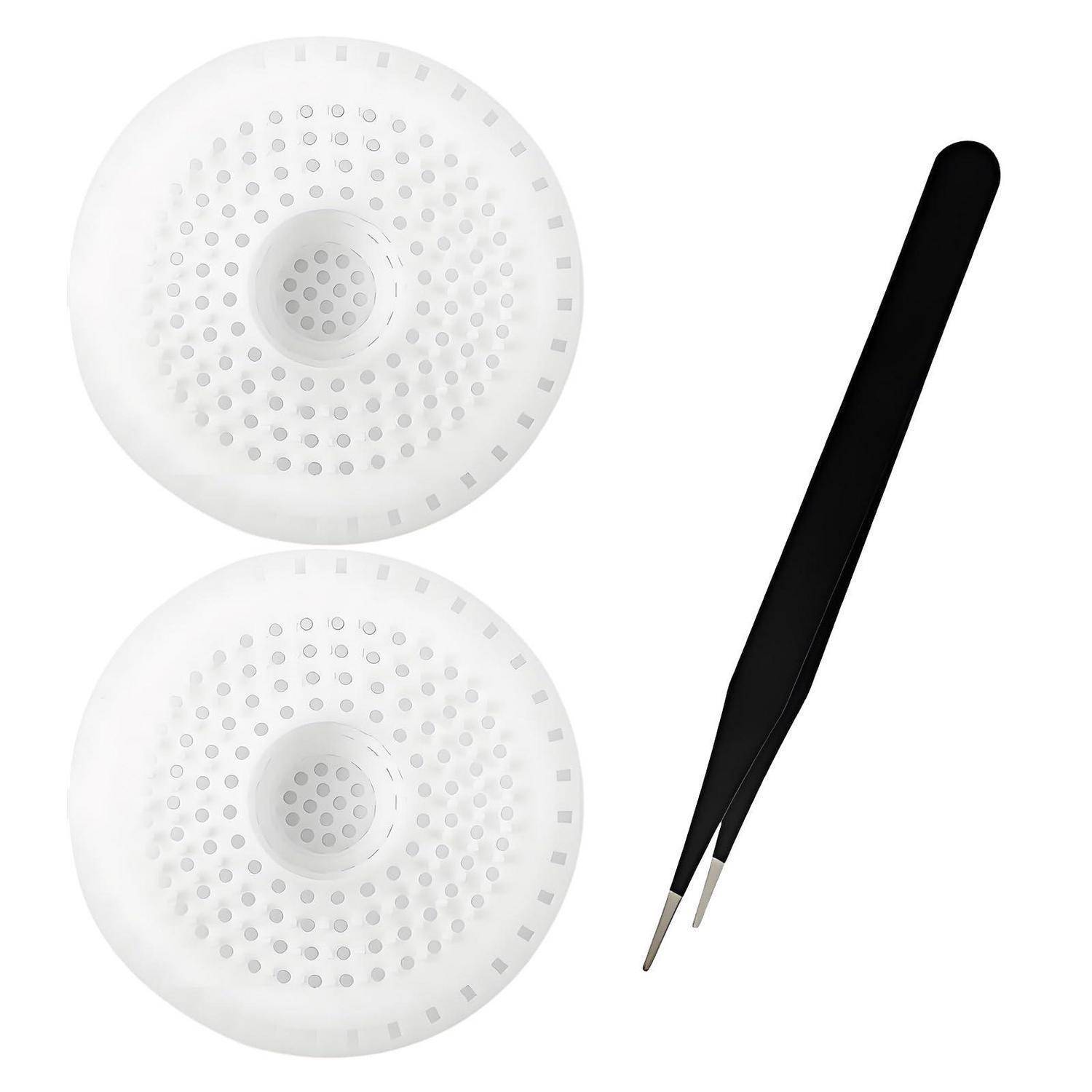 Zwei weiße runde Haftpads mit perforierten Oberflächen neben einem schwarzen pinzettenähnlichen Werkzeug auf weißem Hintergrund.