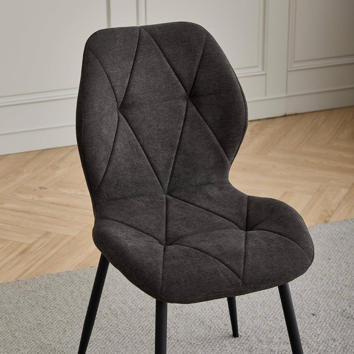 Dunkelgrauer Esszimmerstuhl mit Polsterung, gesteppter Rautensteppung und schwarzen Beinen auf einem hellen Teppich in einem modernen Zimmer.