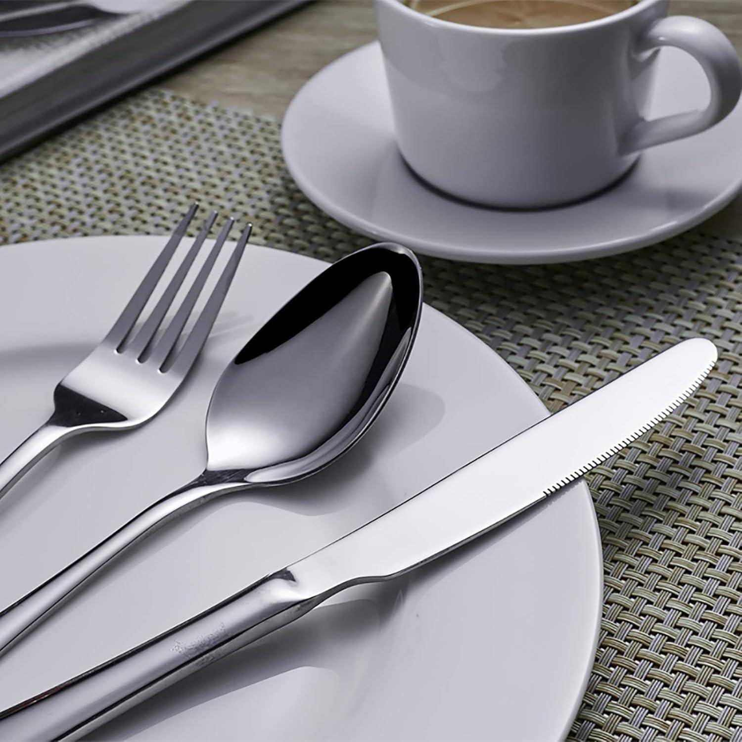 Silbergabel, Löffel und Messer auf einem weißen Teller neben einer Kaffeetasse auf einer Untertasse, alles auf einem geflochtenen Platzset arrangiert.