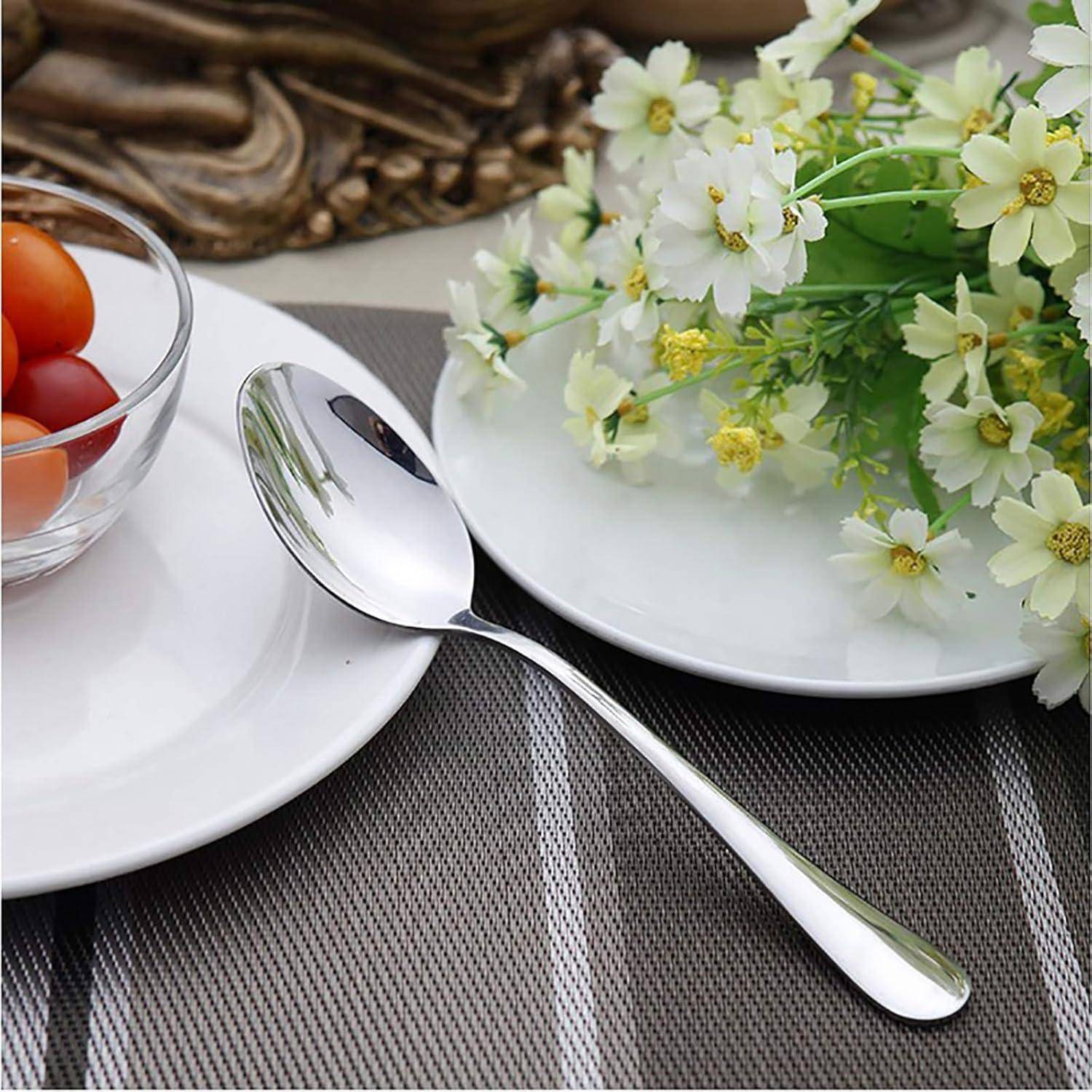 Tischgedeck mit einem Löffel auf einer Platzdecke zwischen weißen Tellern; ein Teller enthält Kirschtomaten, der andere weiße Blüten.