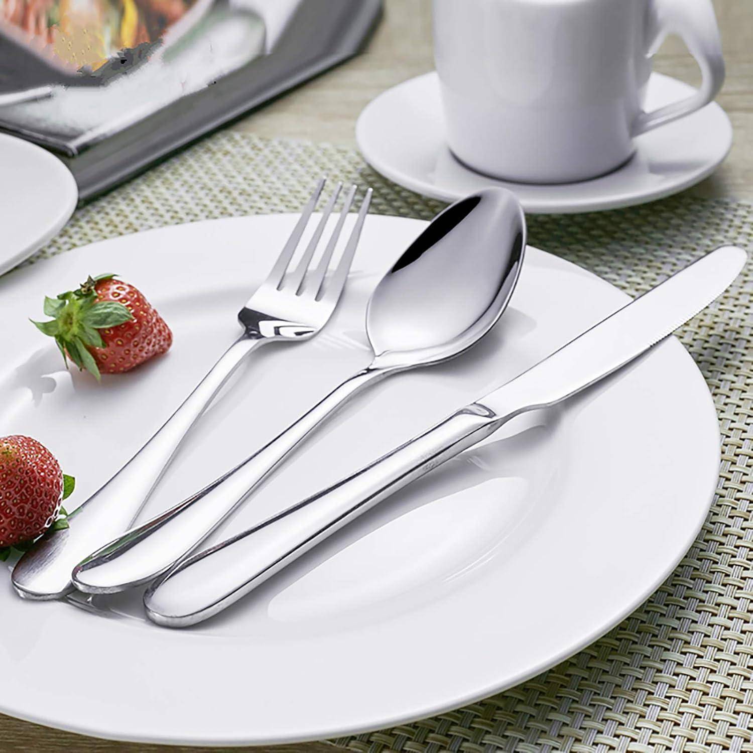 Weißer Teller mit silbernem Besteck (Gabel, Löffel und Messer) neben Erdbeeren in einer Tischdecke mit einer Tasse und Untertasse.