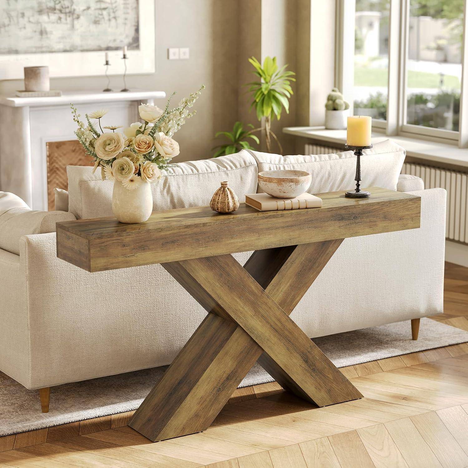 Rustikale Holzkonsole mit X-förmigem Gestell hinter einem Sofa, dekoriert mit einer Blumenvase, einer Schale, Büchern und einer Kerze in einem hellen Wohnzimmer.